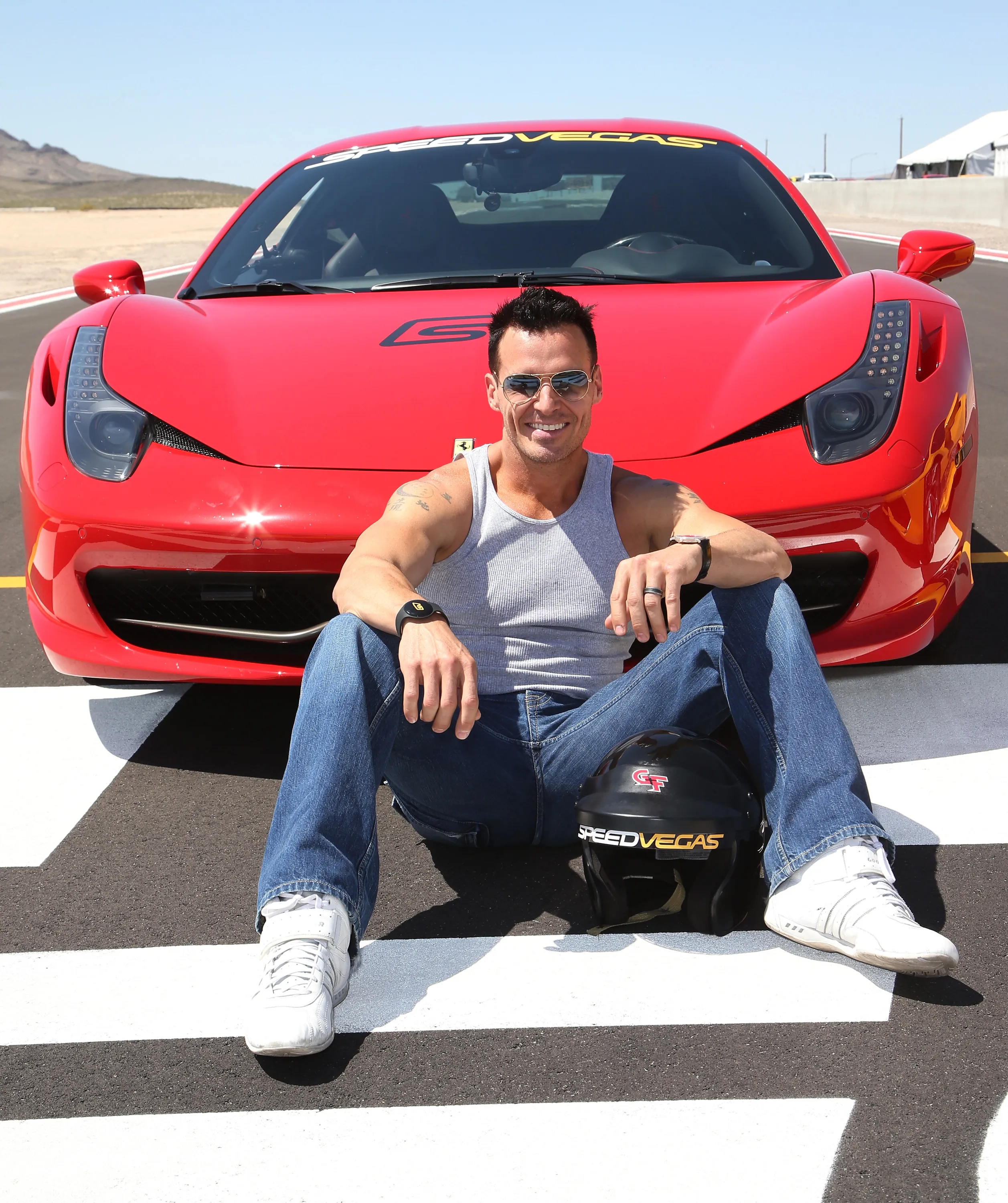 Actor Antonio Sabato Jr. sitting on the ground in front of a red Ferrari.