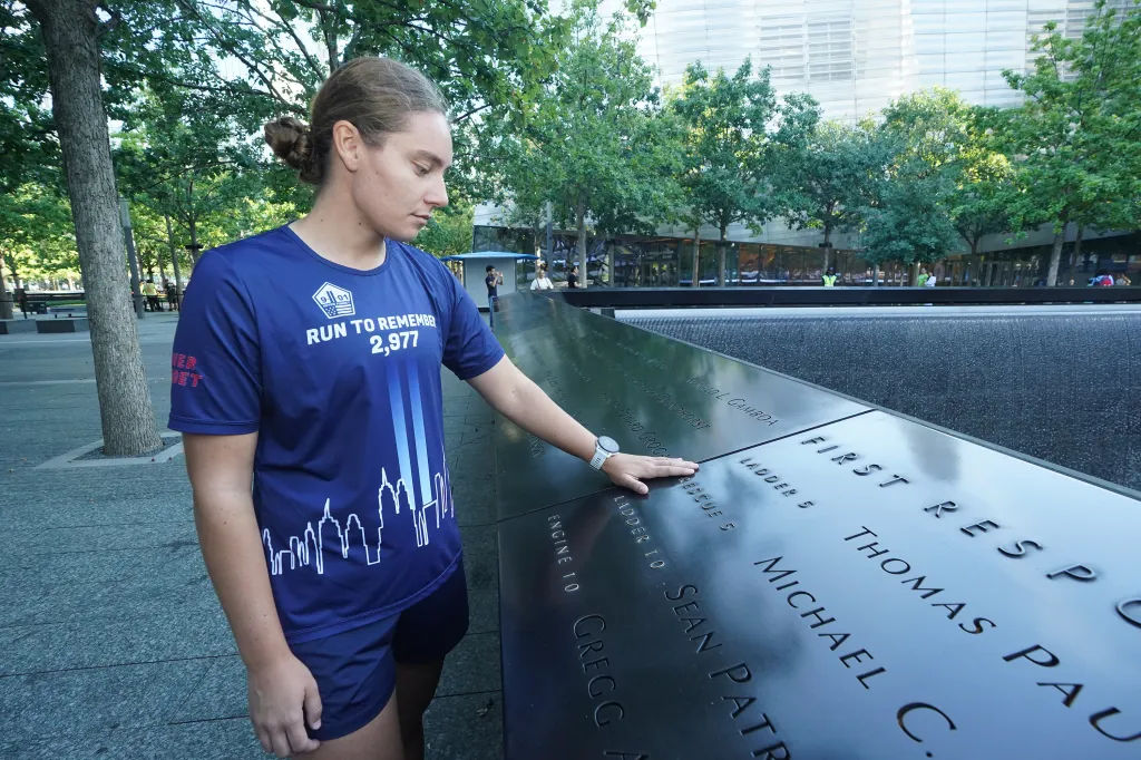 Air Force Capt. Hanna Born, 27, touches the Rescue 5 plaque at the Memorial Tower Pool at Ground Zero on Tuesday, September 8, 2026. Born was 2 years old in the Pentagon's daycare center during the 9/11 attacks and is now running 2,977 miles in honor of those who died that day.
