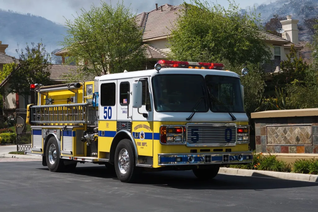 Ventura County Fire Dept. Engine 50 parked on a street with houses and a burned hillside in the background.