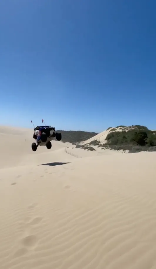 A dune buggy jumps in the air over sandy dunes.