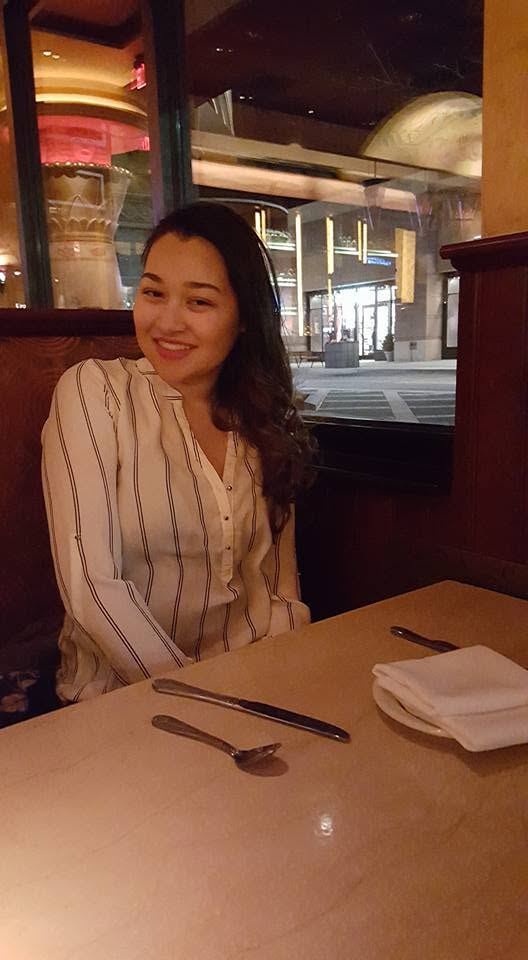 A smiling woman in a striped shirt sitting at a table in a restaurant.