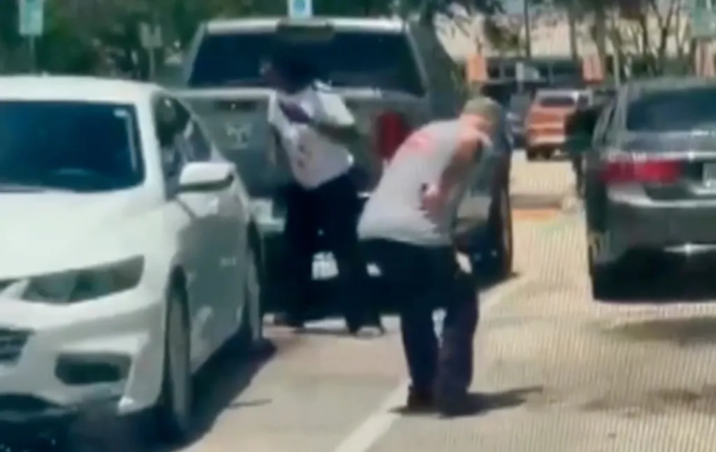 Surveillance video still shows a man in a white shirt and a man in a grey shirt in a confrontation between parked cars.