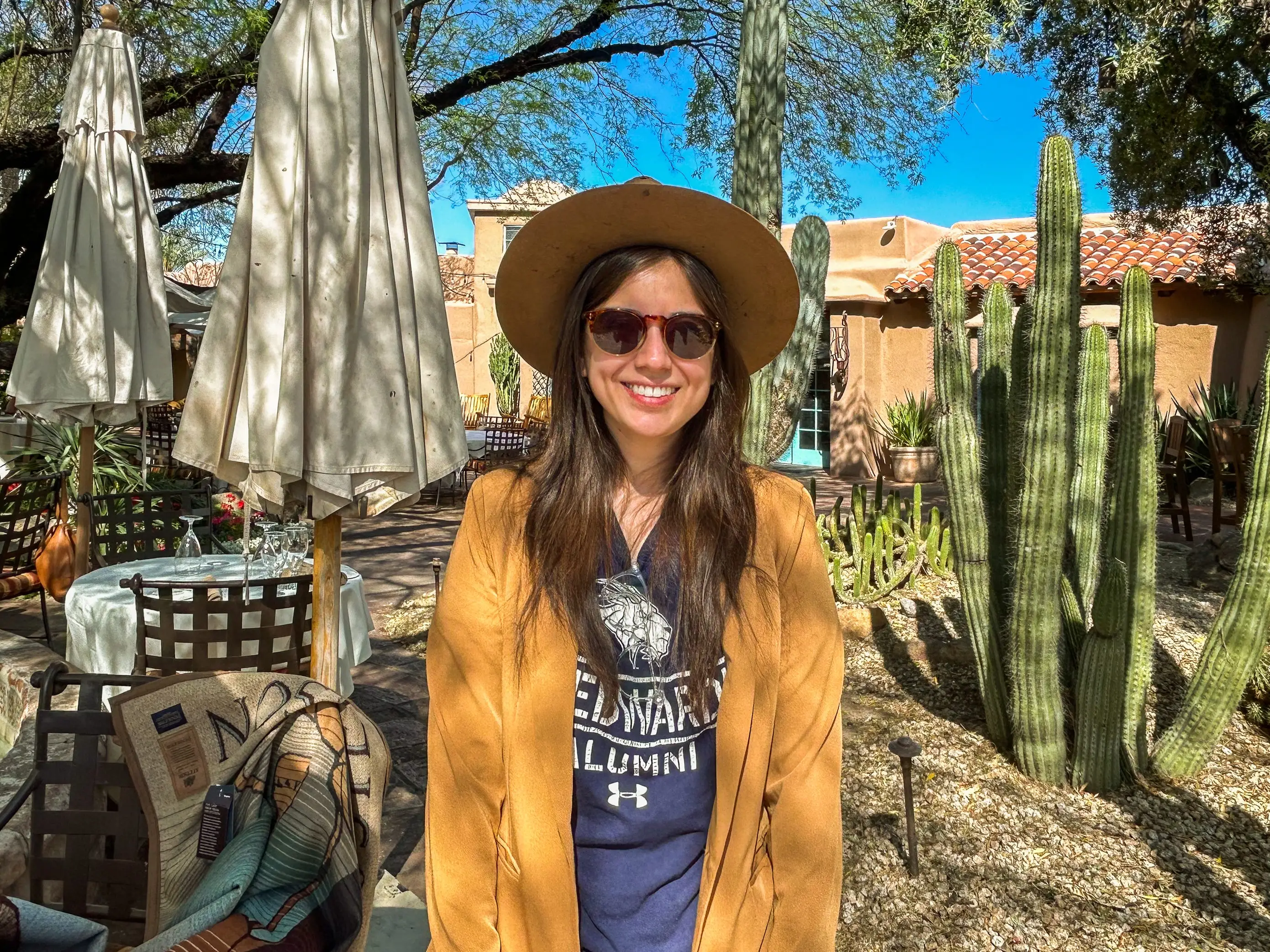 The author in a cowboy hat and sunglasses stands smiling in front of cacti and an adobe building in Scottsdale