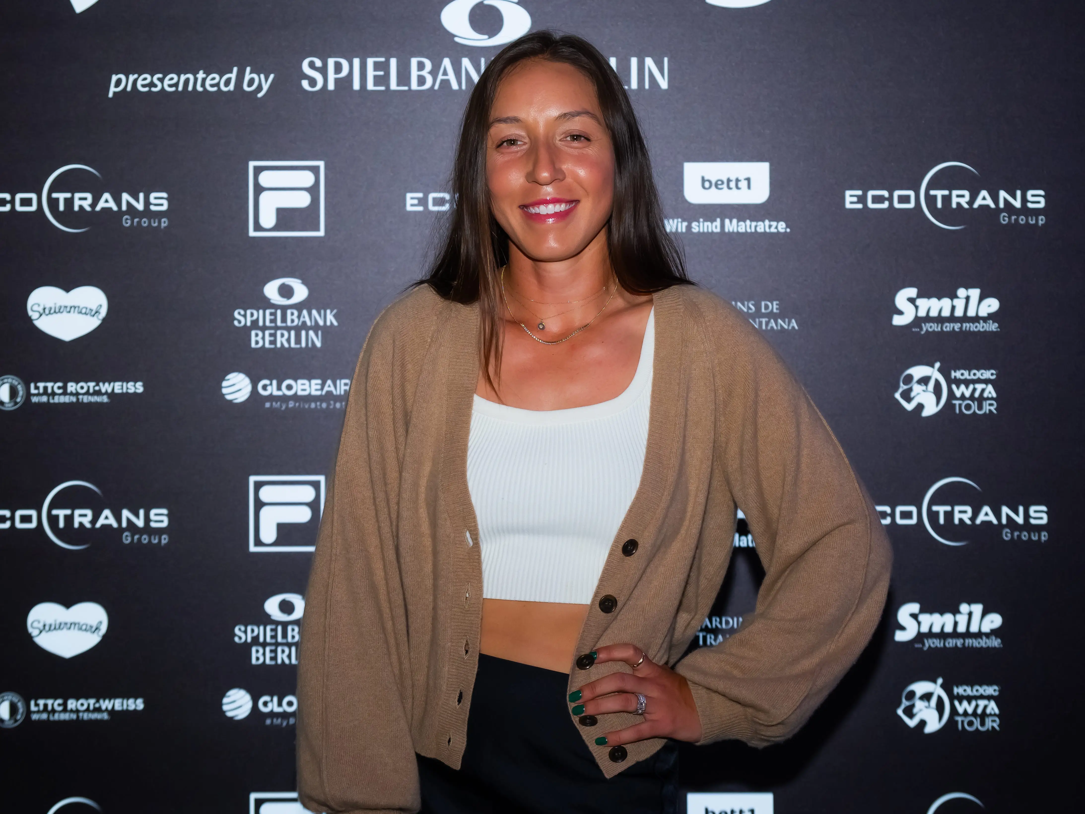 Jessica Pegula poses in a light brown cardigan and white cropped tank top for day one of the Ecotrans Ladies Open Berlin 2024.