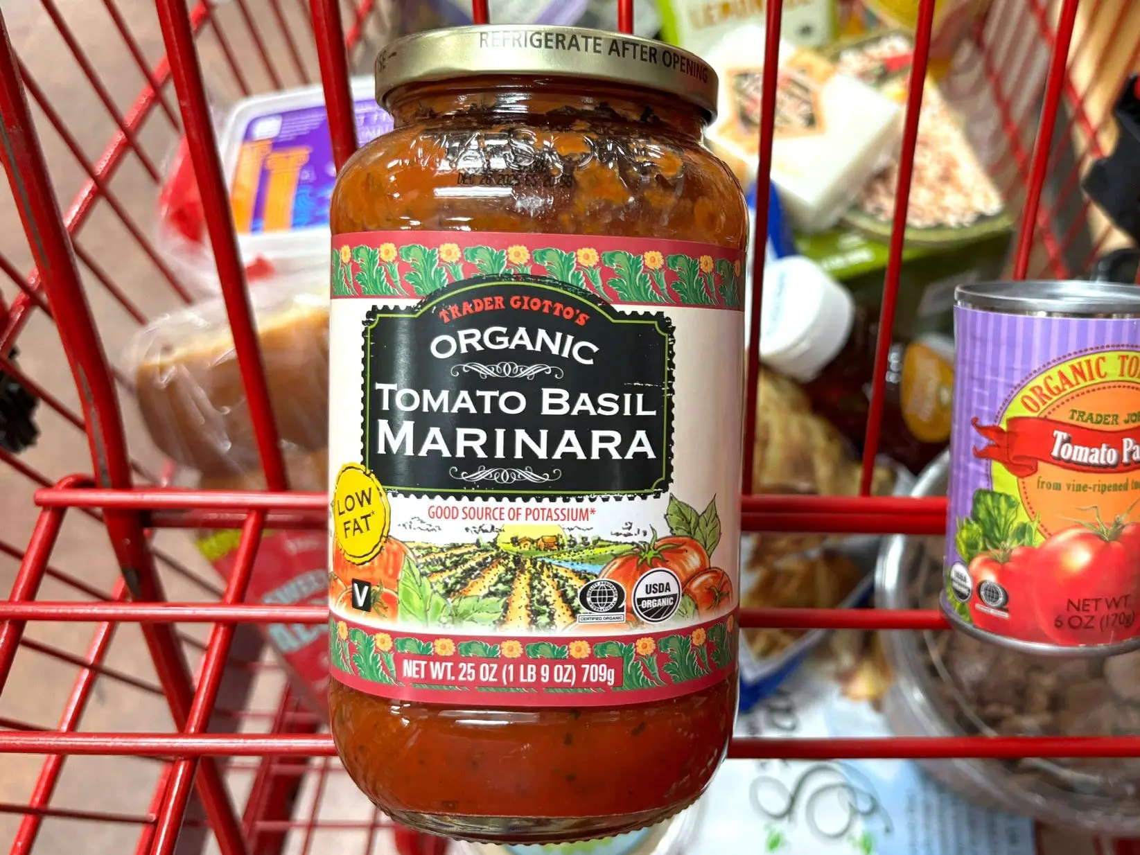 A jar of Trader Giotto's organic tomato-basil marinara sauce in a red shopping cart.