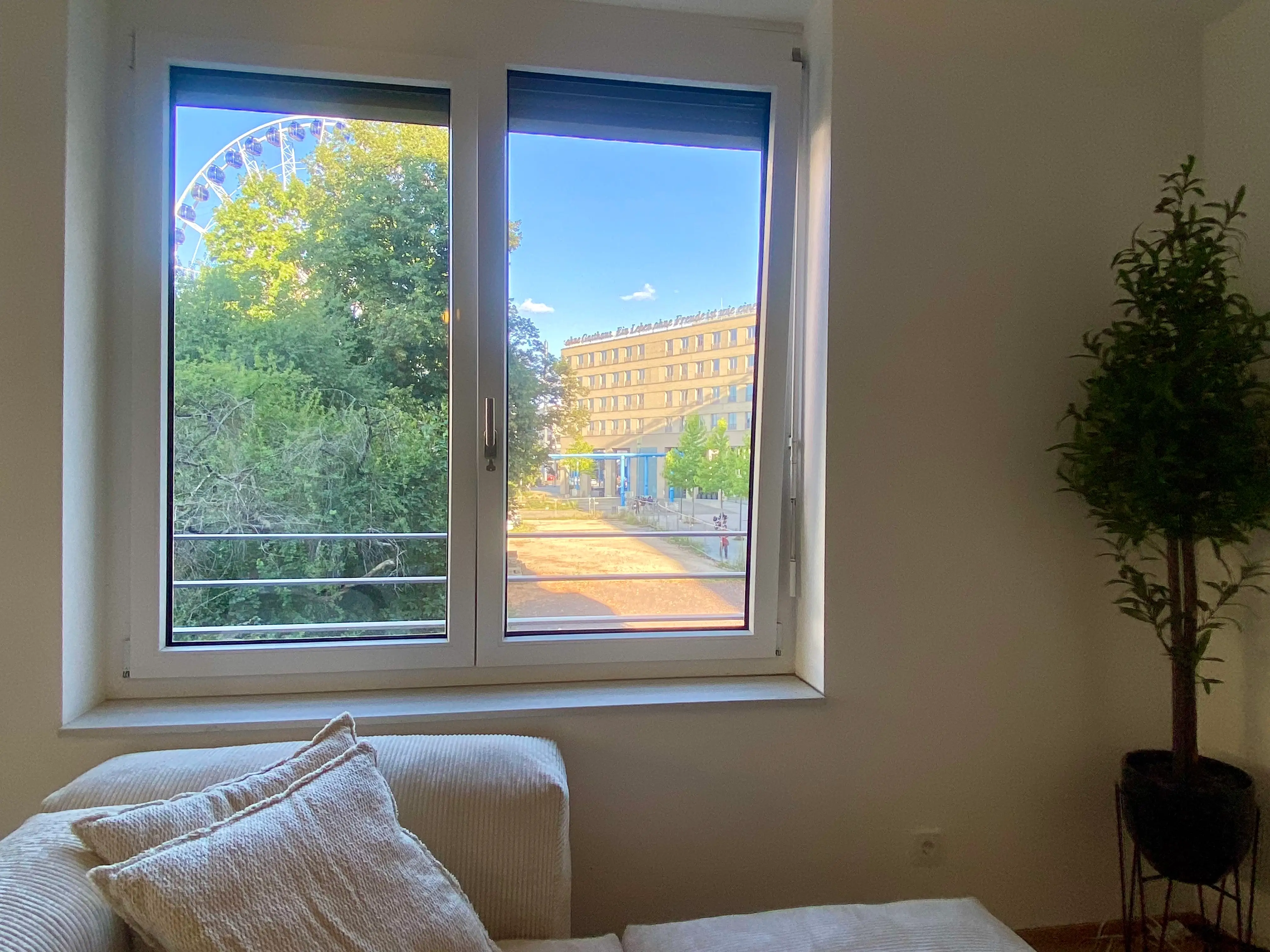A view of a Ferris wheel covered by a tree from a window in an apartment in Germany.