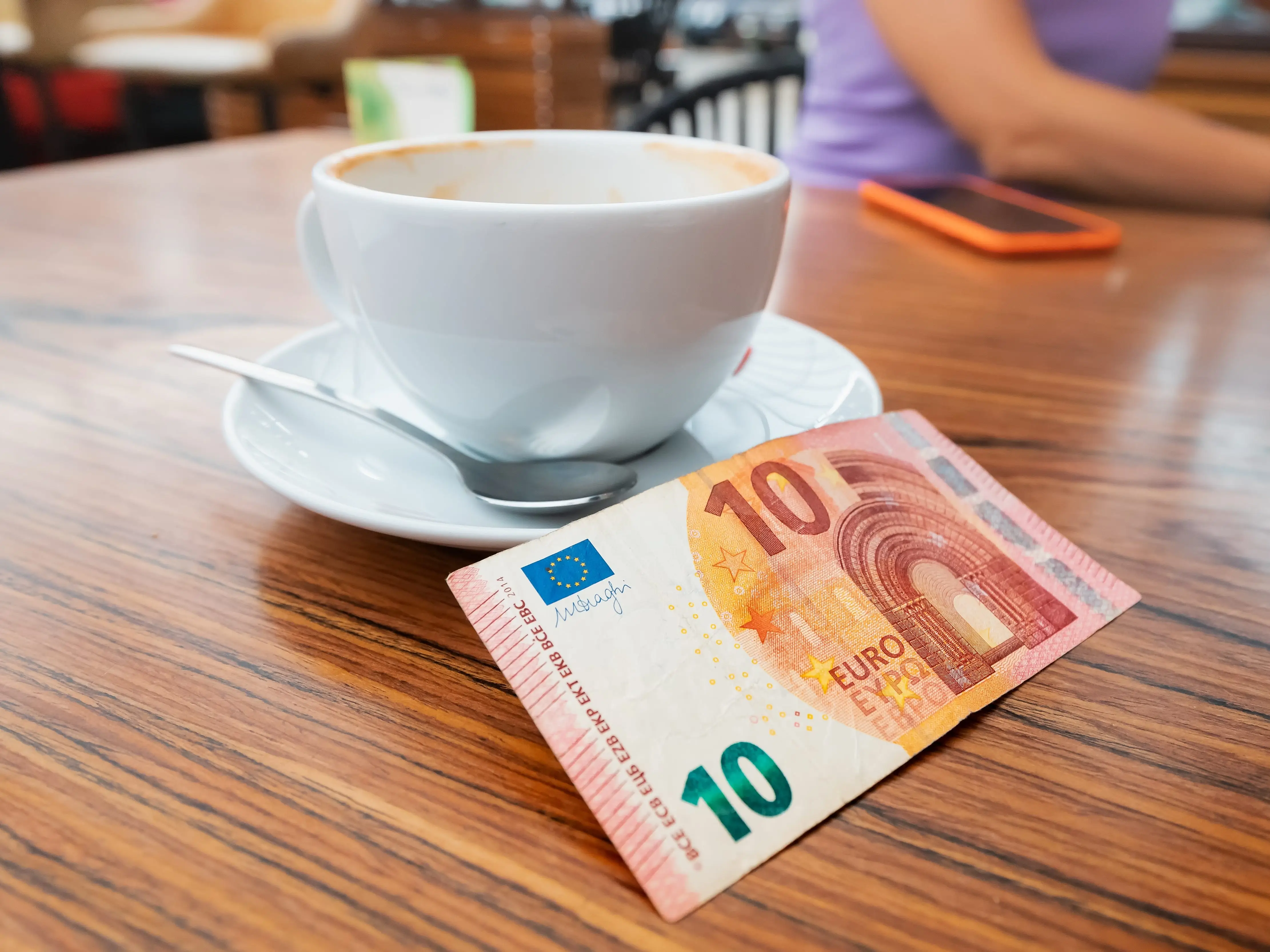 A 10 euro bill next to a tea cup on a wooden table.