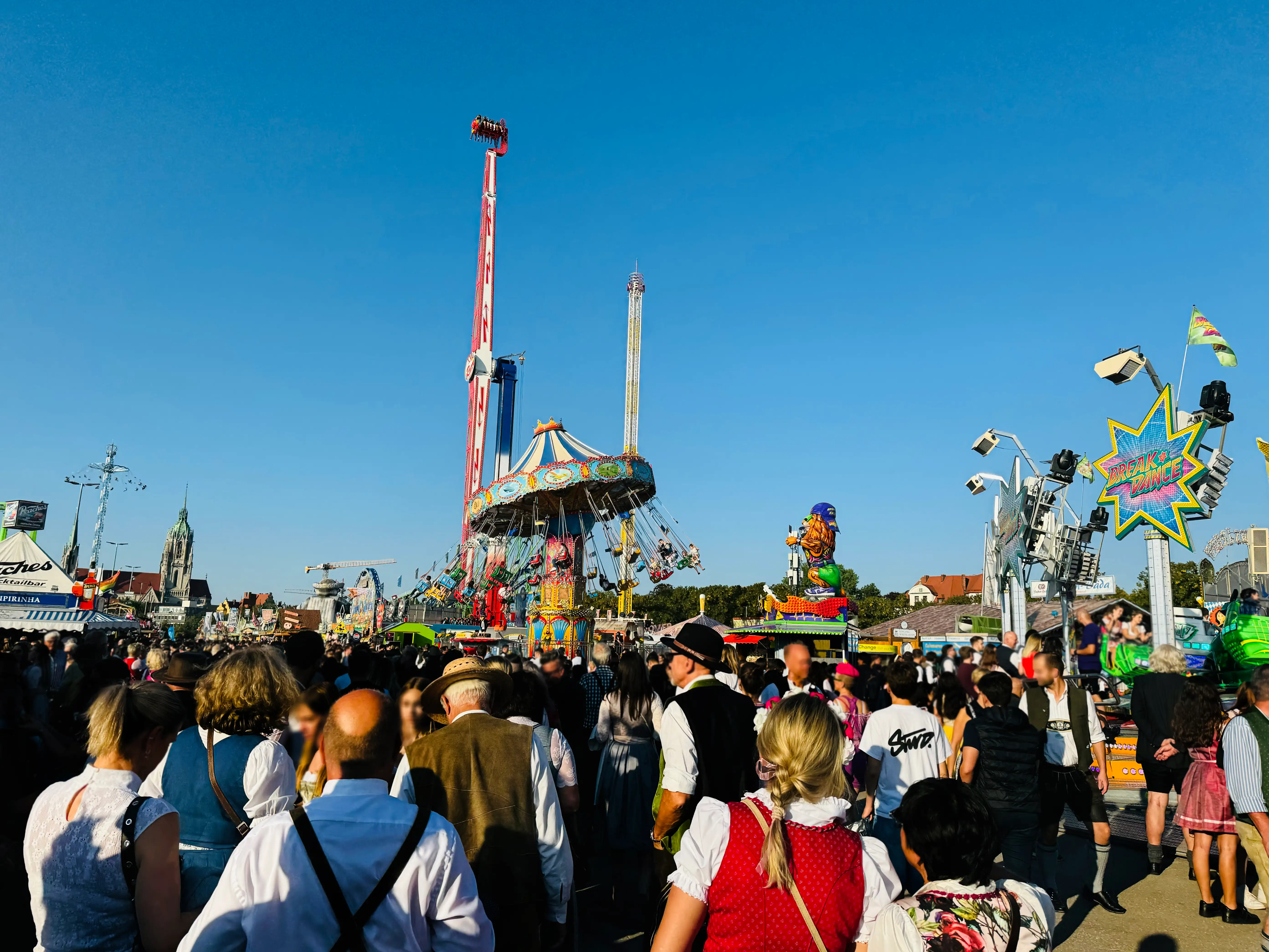 A large crowd of people walking around a carnival with amusement rides.