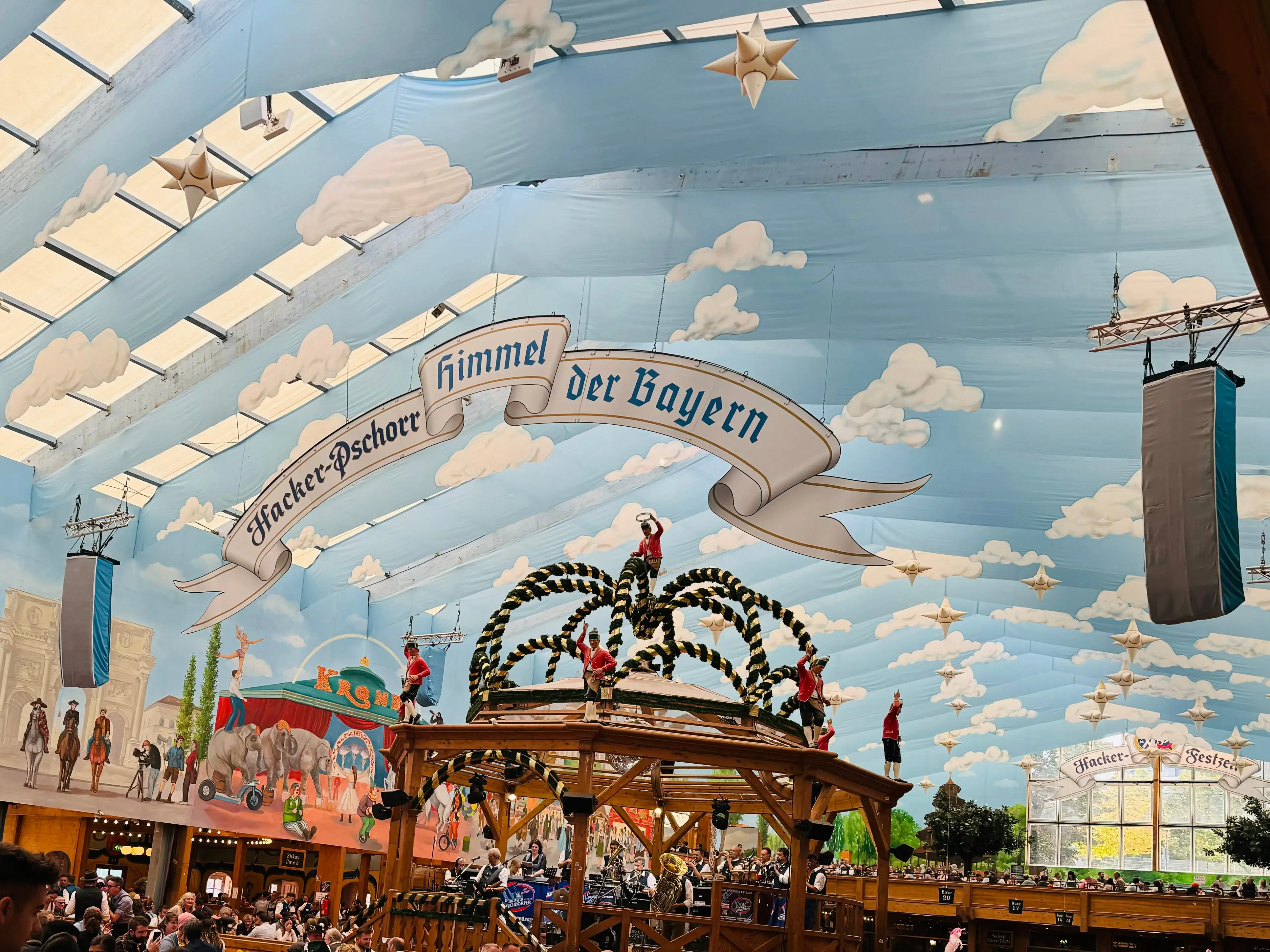 The interior of a tent with artwork that resembles a sky, people and horses in a town, and a banner in German.