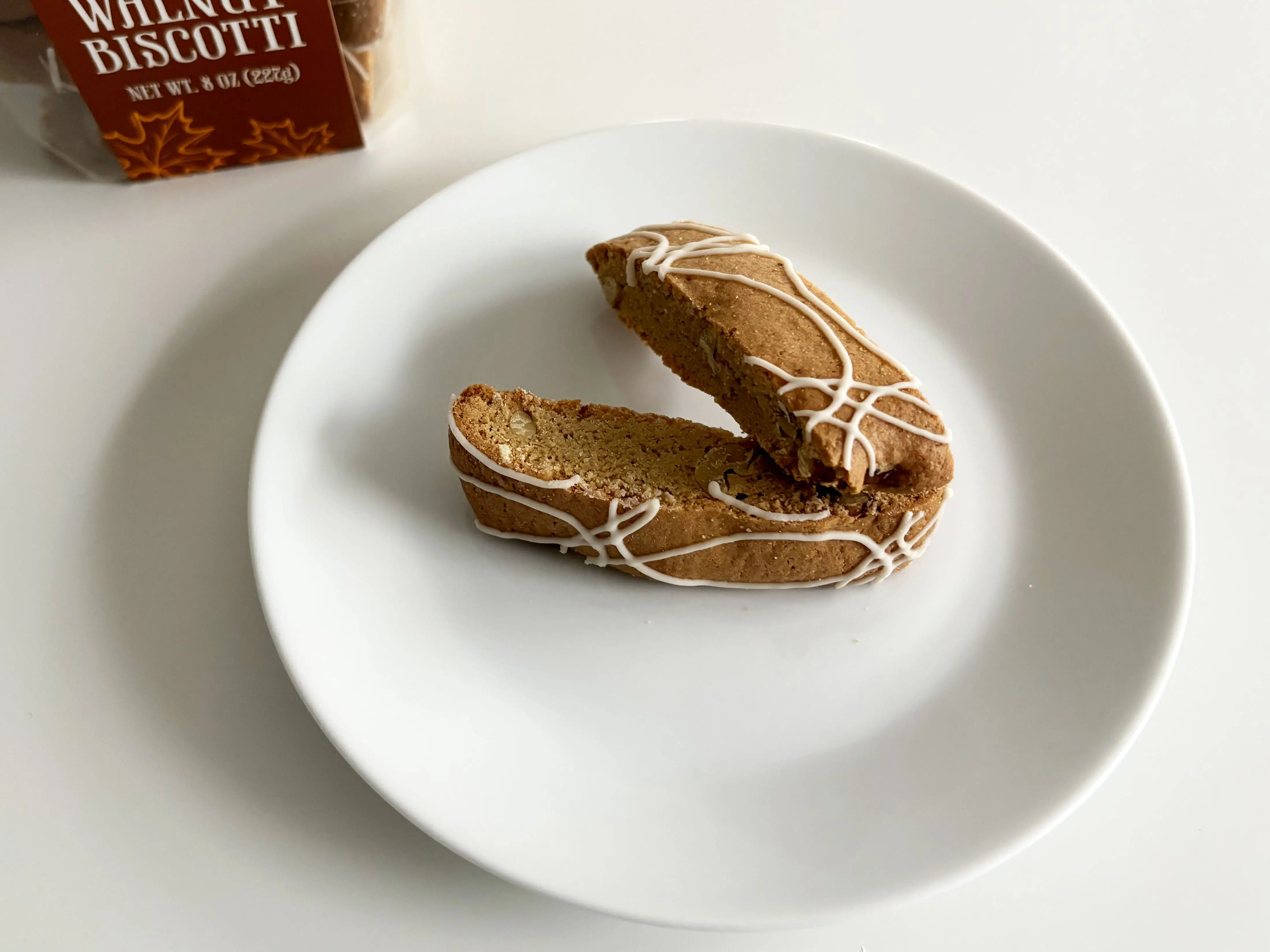 Trader Joe’s mini maple-walnut biscotti on a white plate next to a plastic box of the cookies.