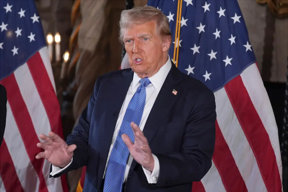 President -elect Donald Trump gestures as he speaks, in front of two American flags, during a press conference at Mar-A-Lago on December 16, 2024.