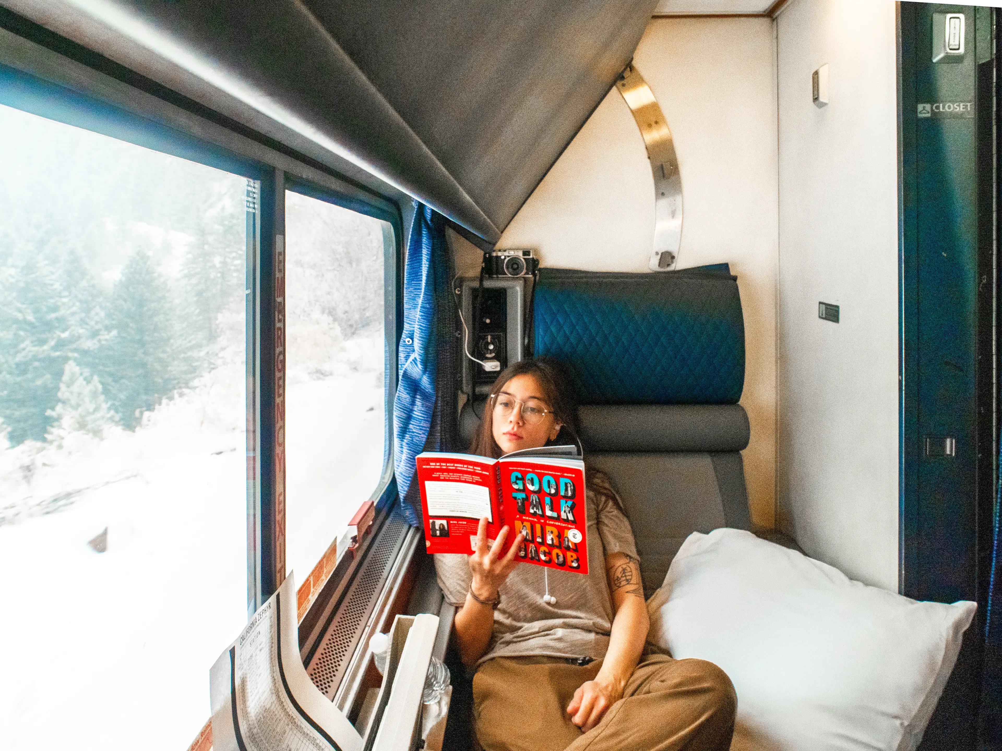 The author sits reading in a train cabin with a window on the left