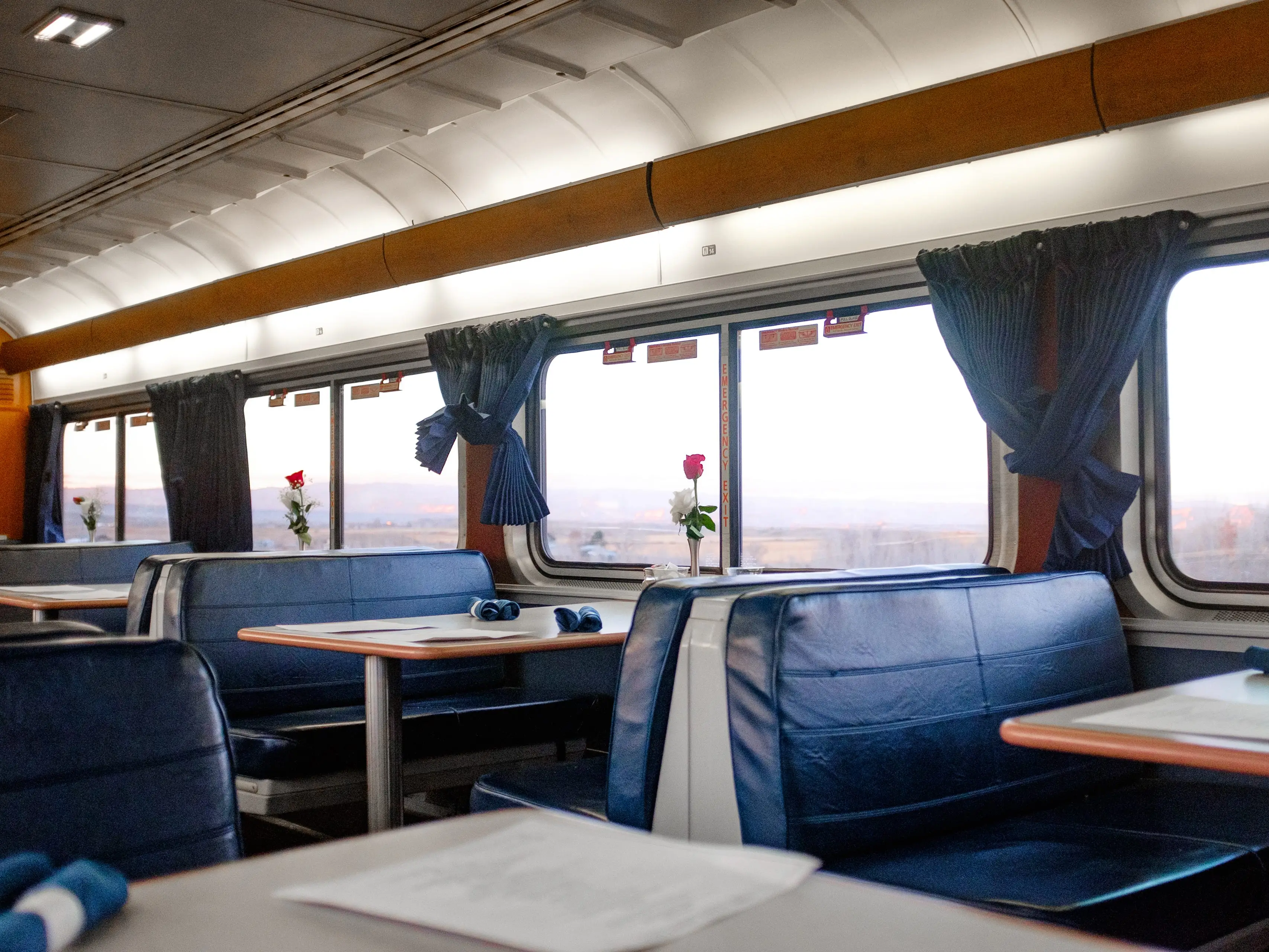 Inside a train dining car at sunset with red canyons out the window and booths with roses on them