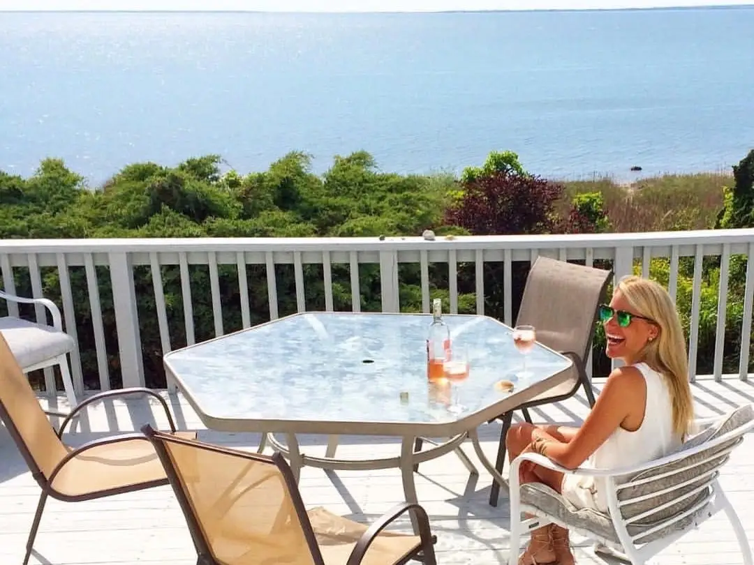 Author Katherine Parker-Magyar sitting at a glass table on a balcony overlooking water in Montauk