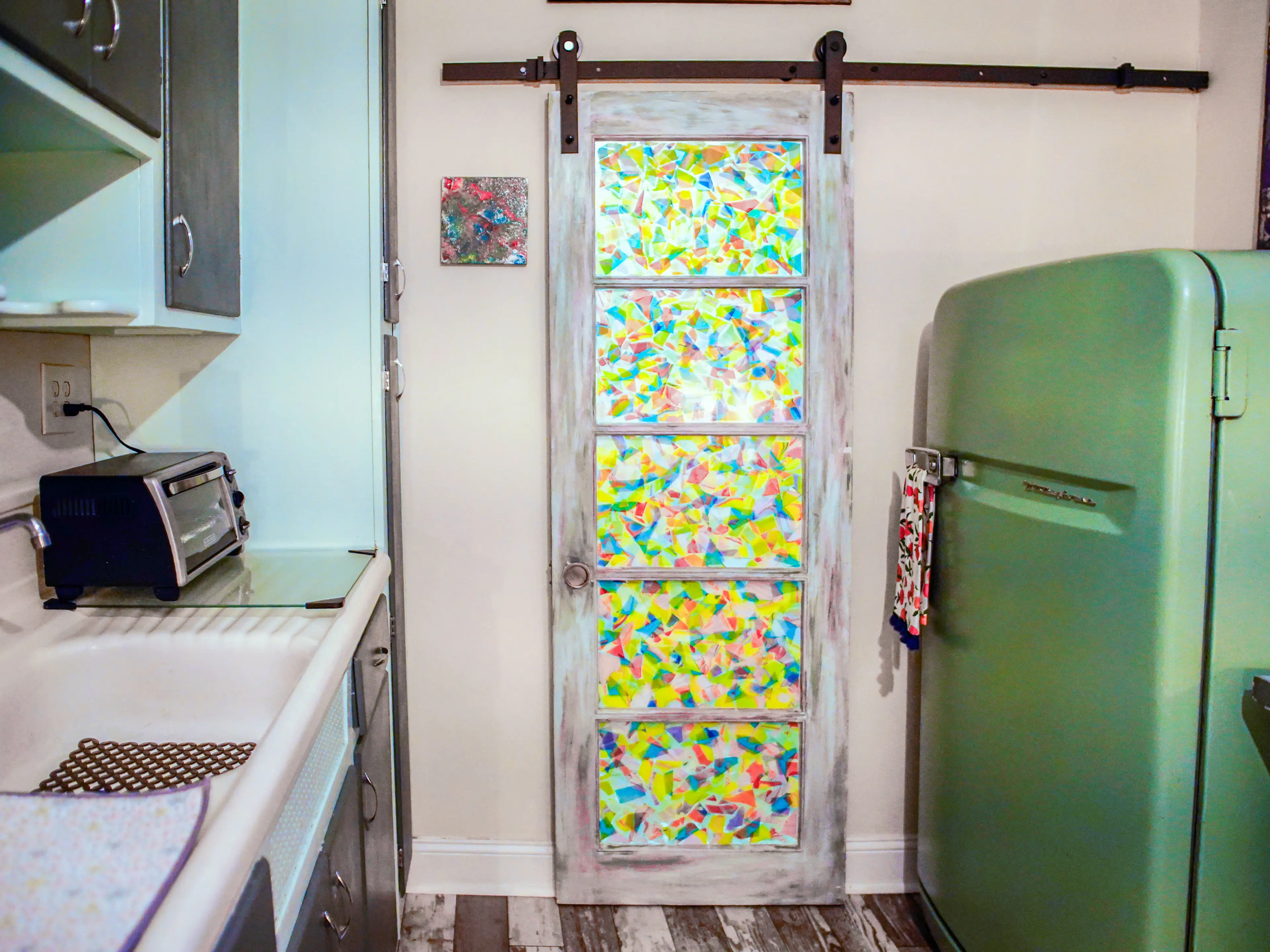 Inside the tiny home kitchen. there's a green fridge on the right, a sink and counter on the left, and a mosaic sliding door in the center