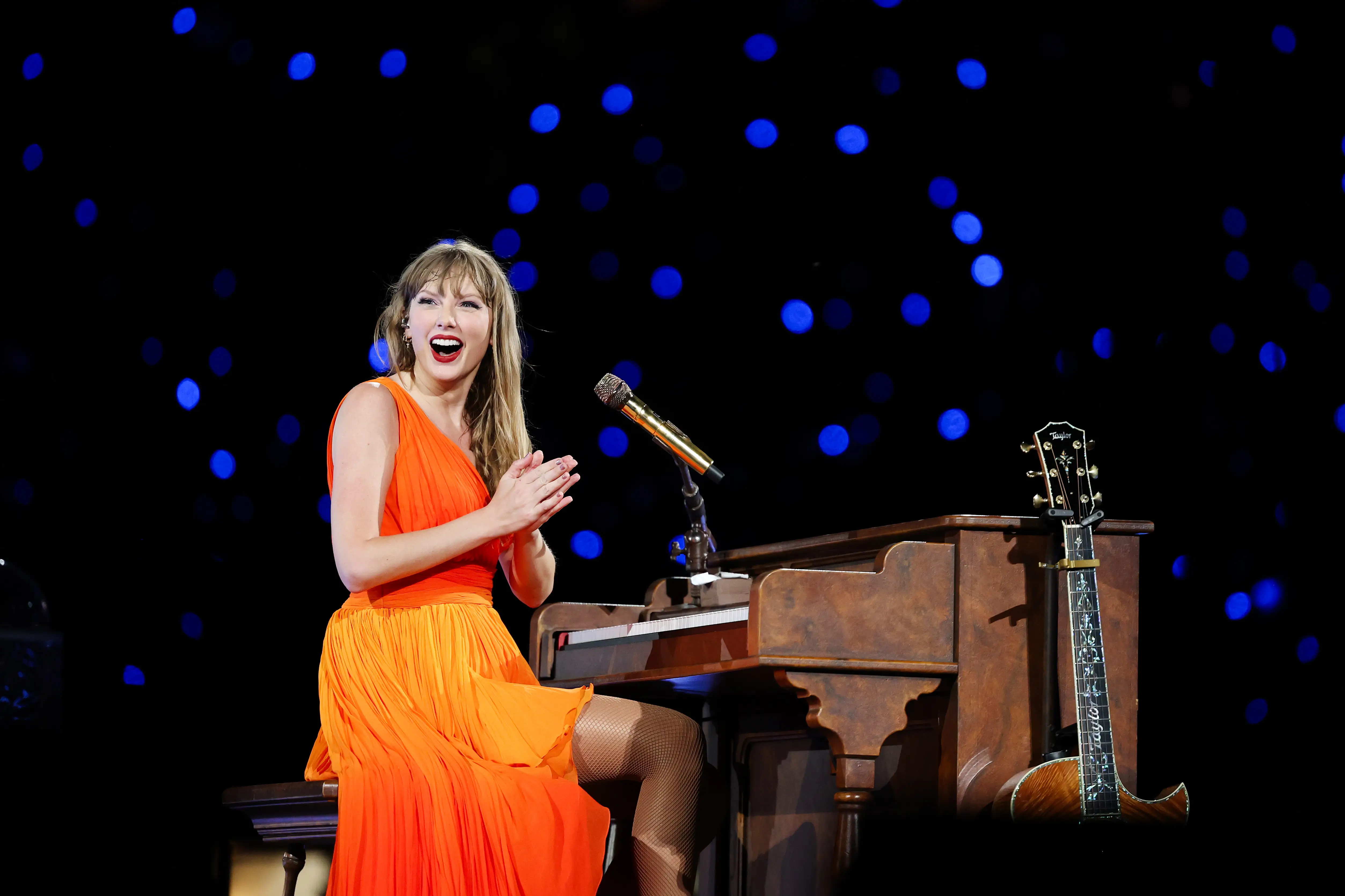 Taylor Swift wears an orange dress onstage at the Eras Tour.