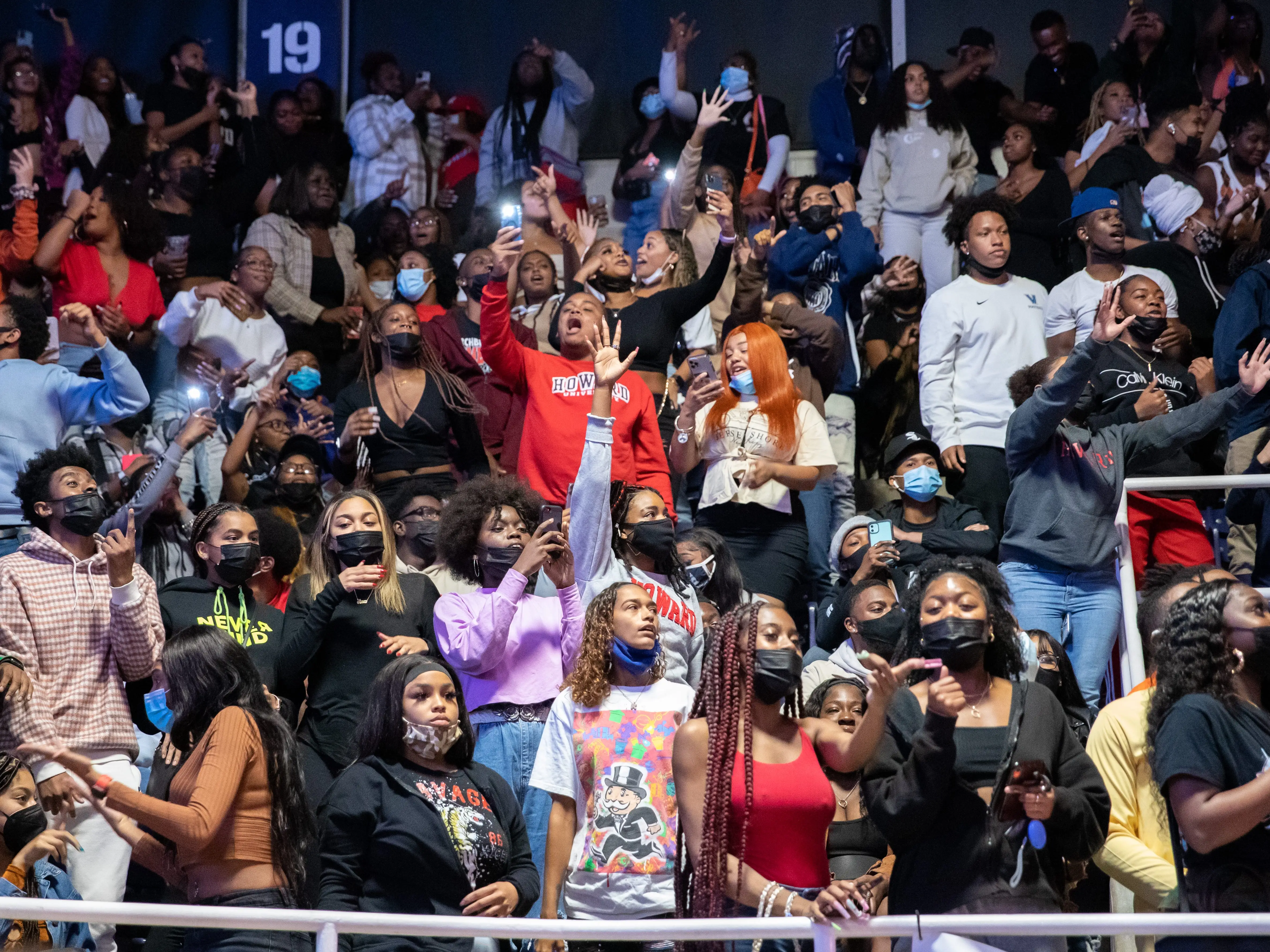 A crowd of college students cheering, some of whom are recording videos on their phones.