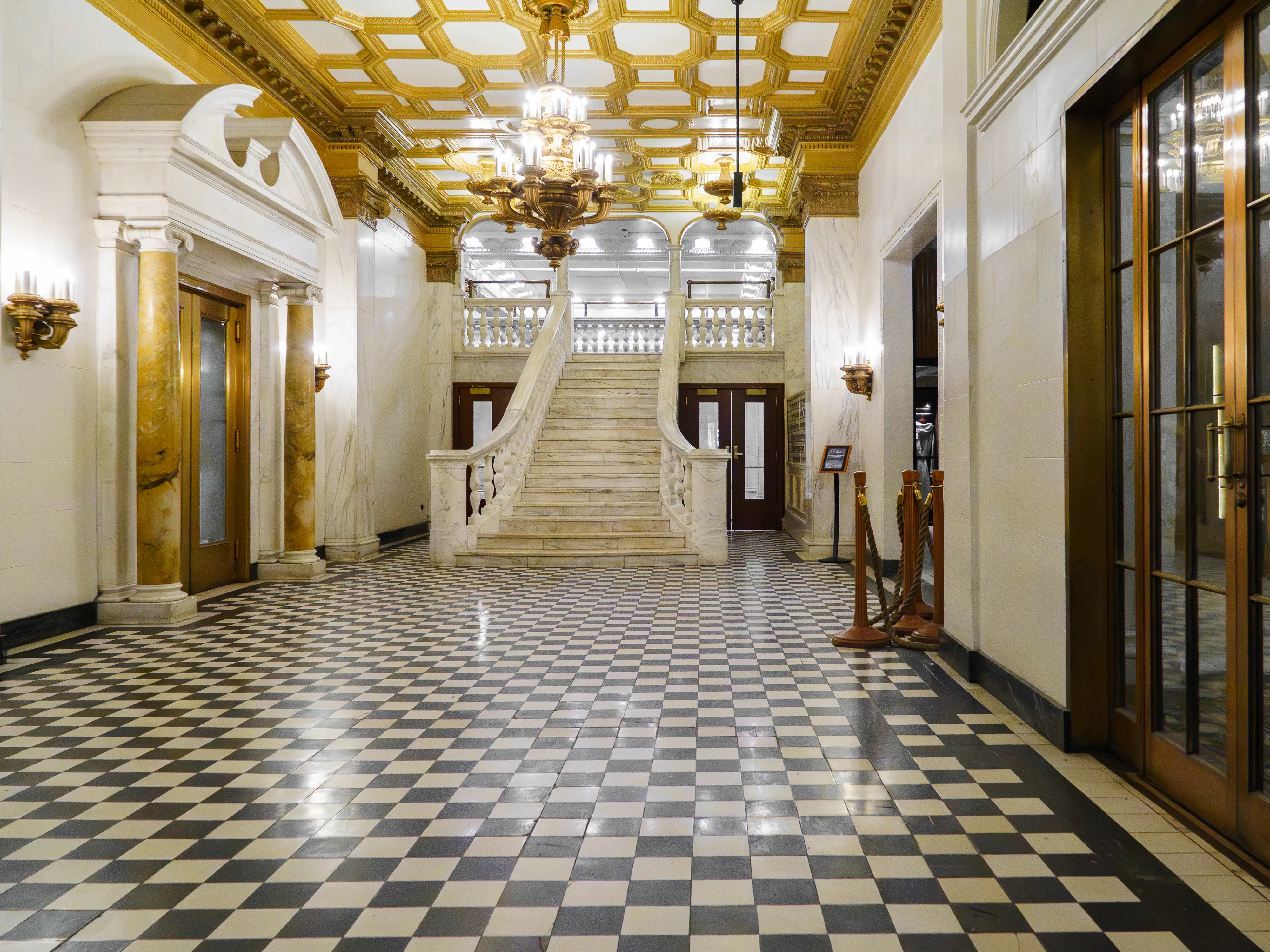 Inside the hotel, a grand marble staircase at the back of a bright, empty hall with gold moldings on the ceilings