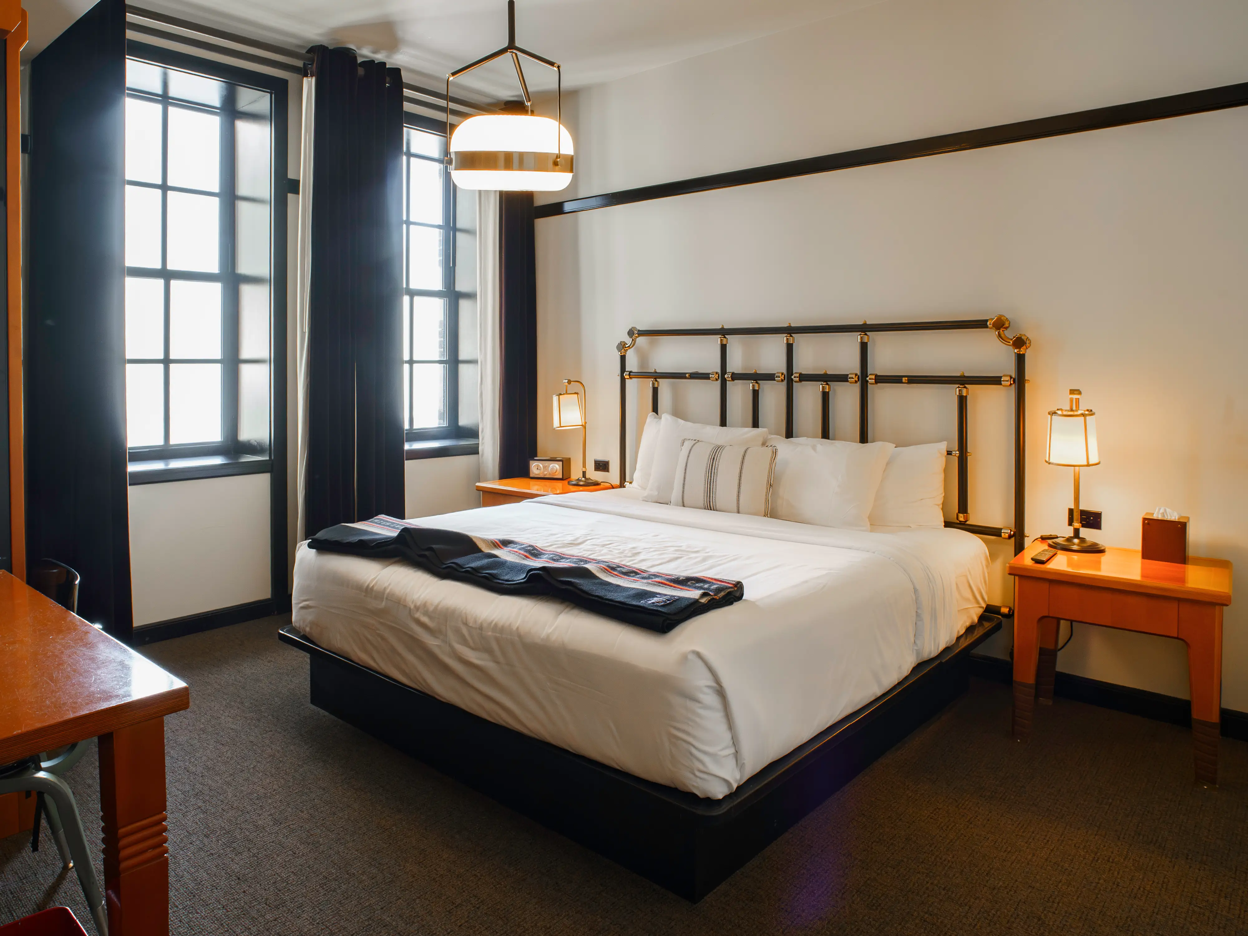 Inside a room at the Chicago Athletic Association, there's a bed in between two nightstands and two windows on the left wall