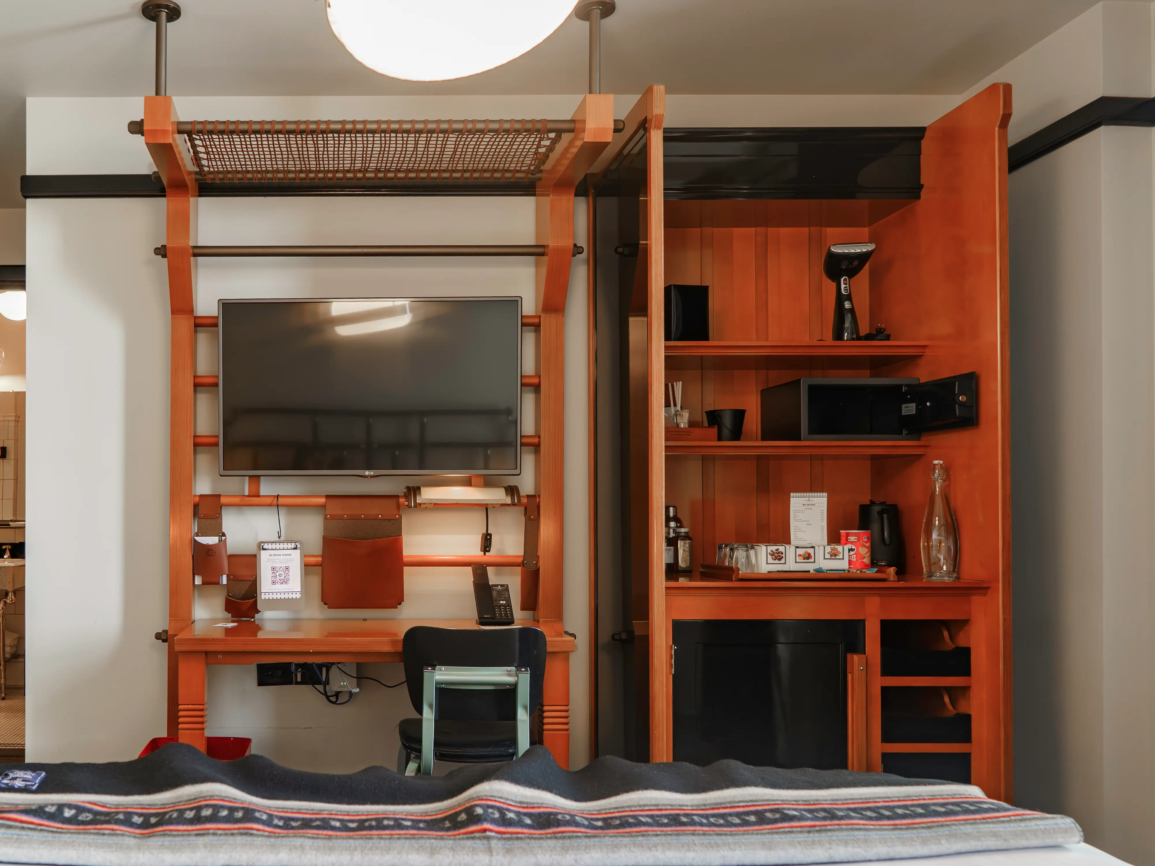 A desk, TV, and bar in front of the bed in the hotel room