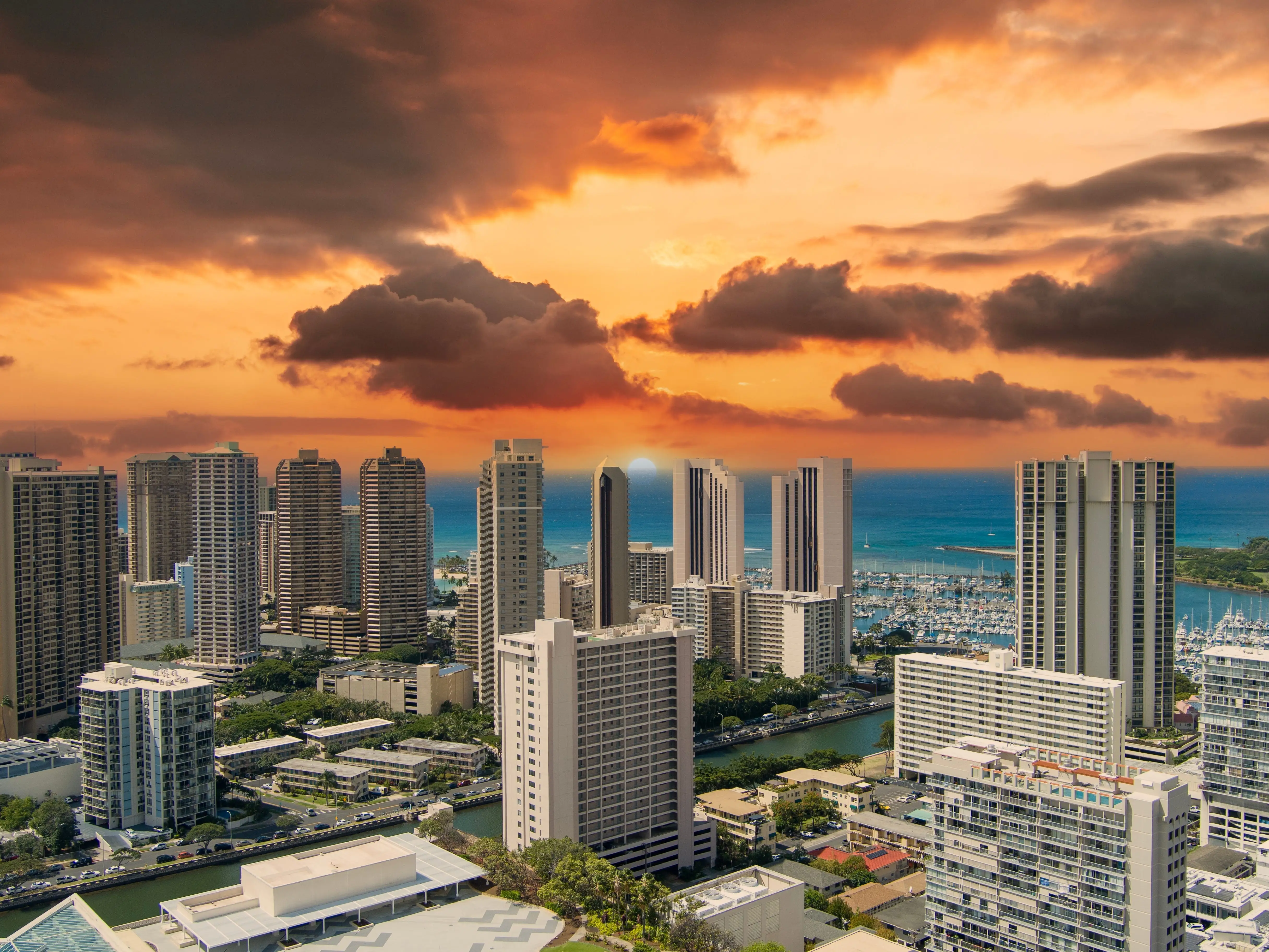 aerial shot of the Ala Wai Canal with skyscrapers, hotels and condos, lush green trees and cars driving on the street, boats and yachts in the harbor in Honolulu Hawaii USA