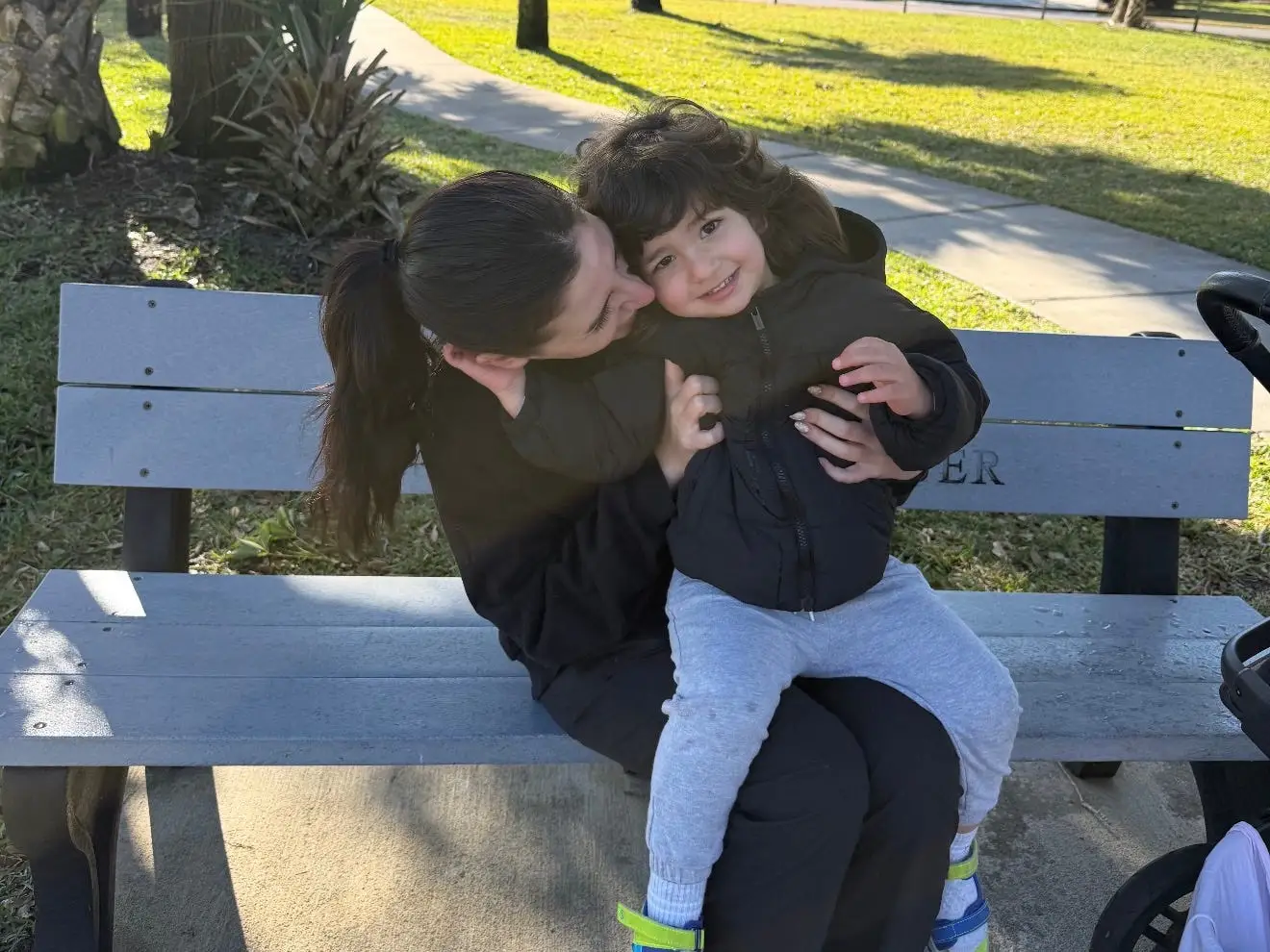 Woman kissing child's cheek on a park bench