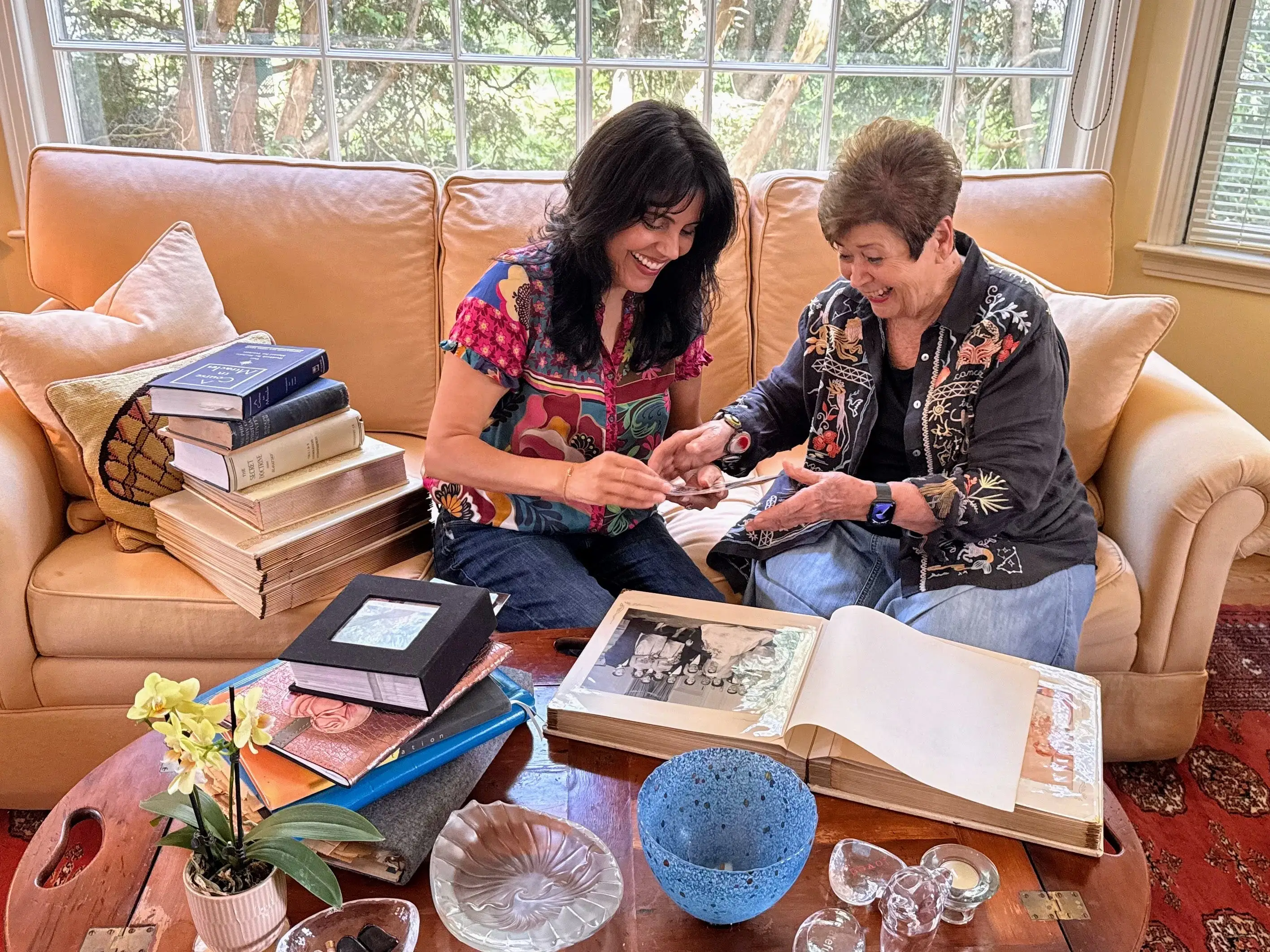 Two women sitting together on couch, going through books and photos