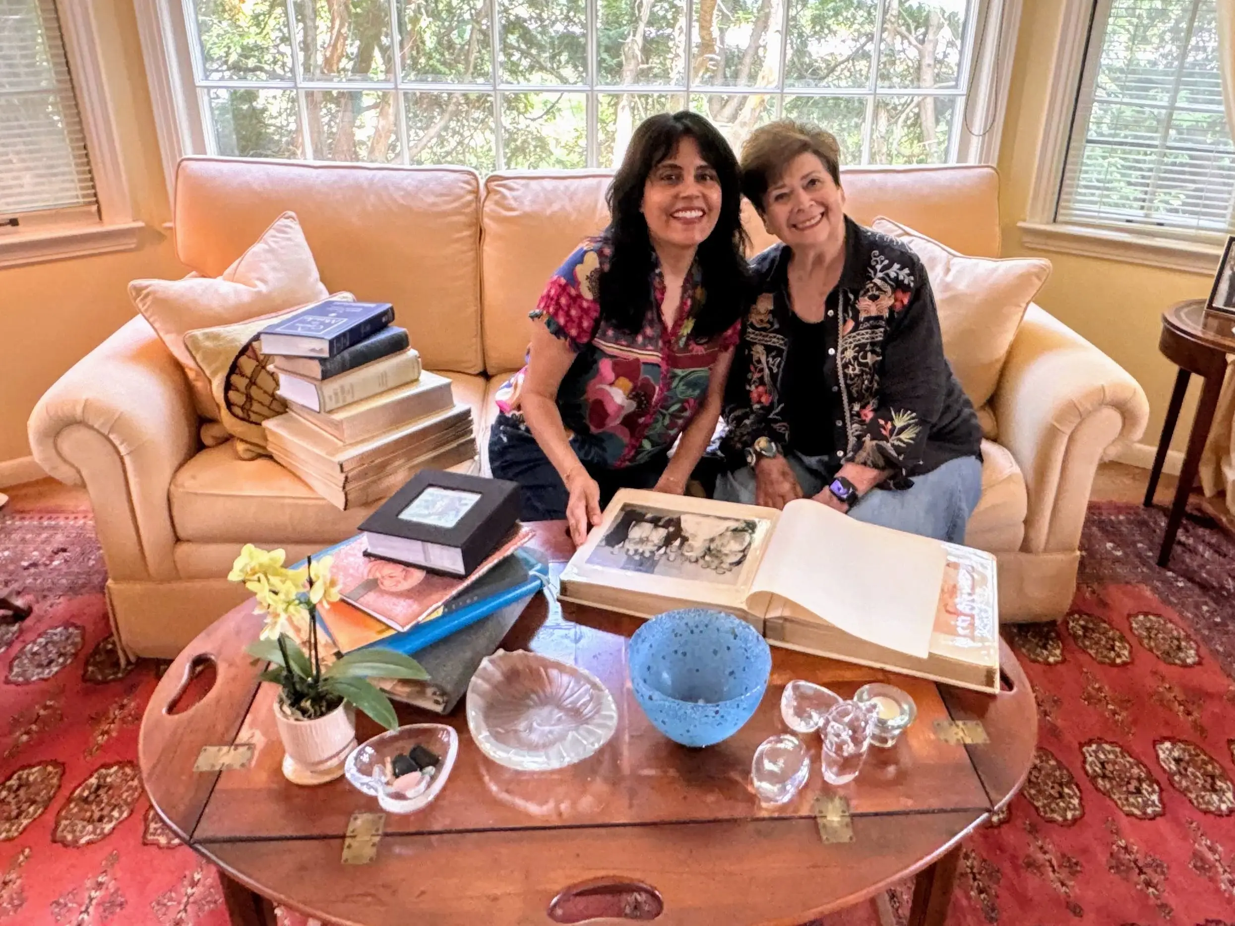 Two women sitting on couch behind piles of books, other objects