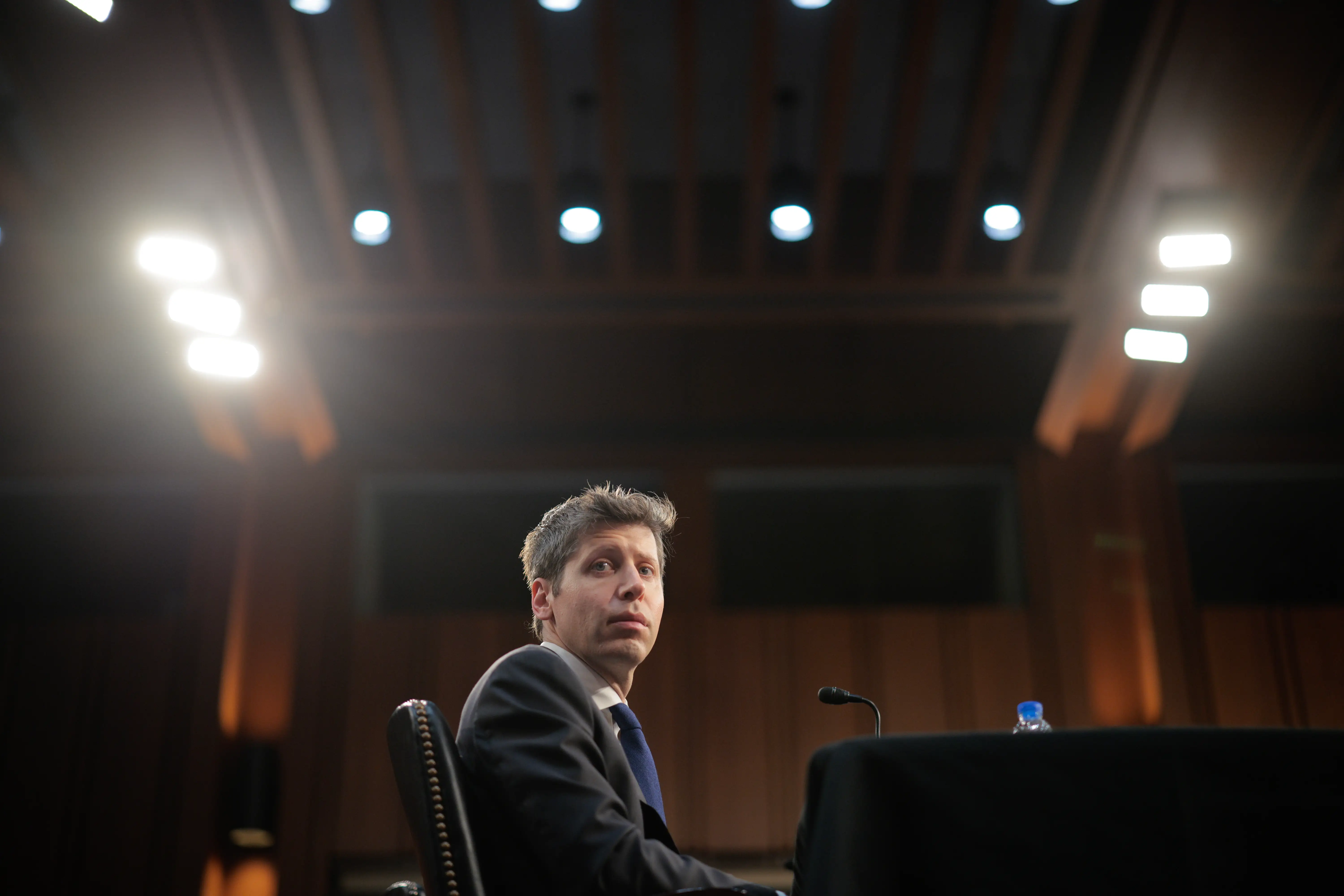 Sam Altman, CEO of OpenAI, sits at a black table with a small black mic.