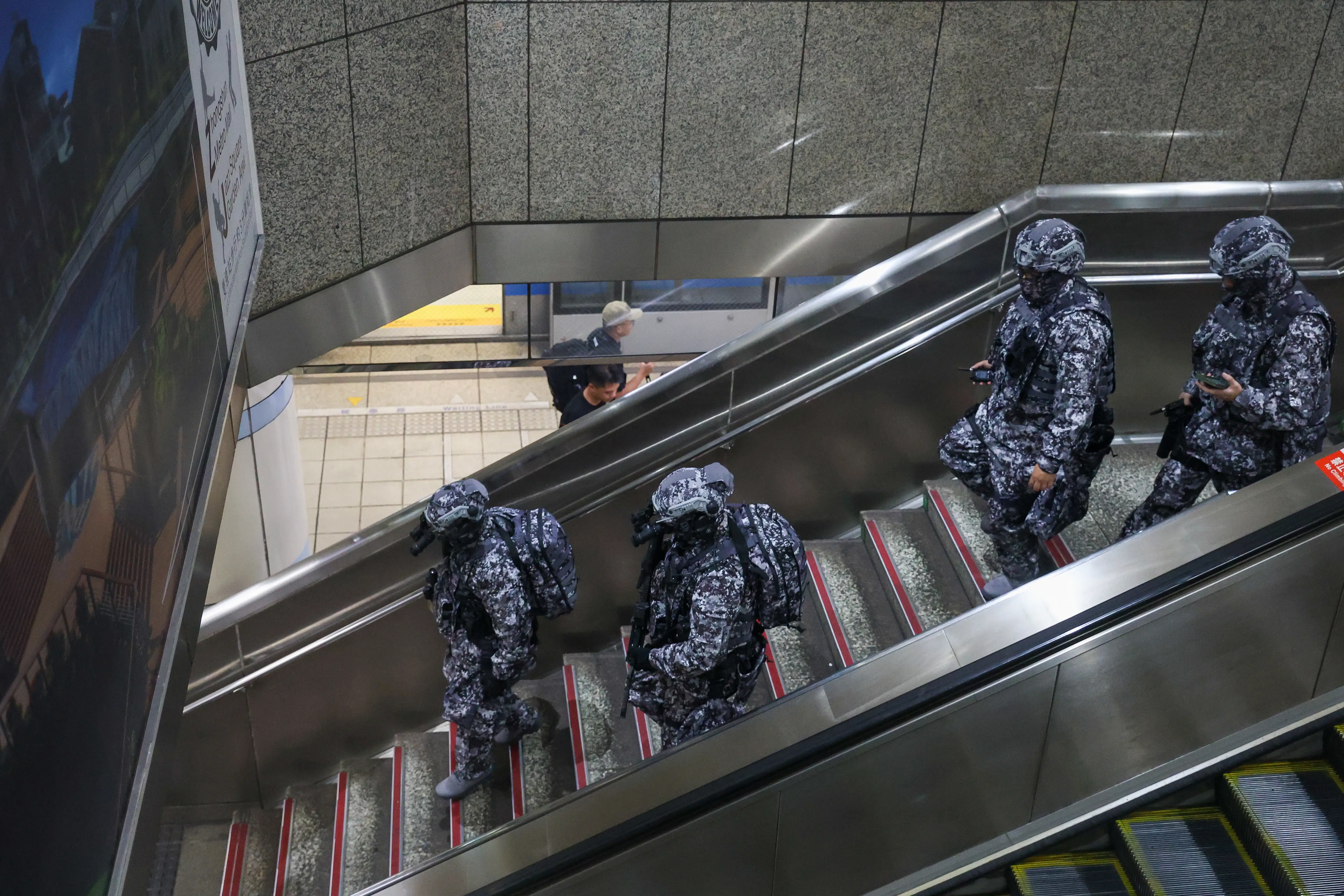 Four Taiwanese soldiers in digital camouflage walk down a flight of stairs in an underground subway station.
