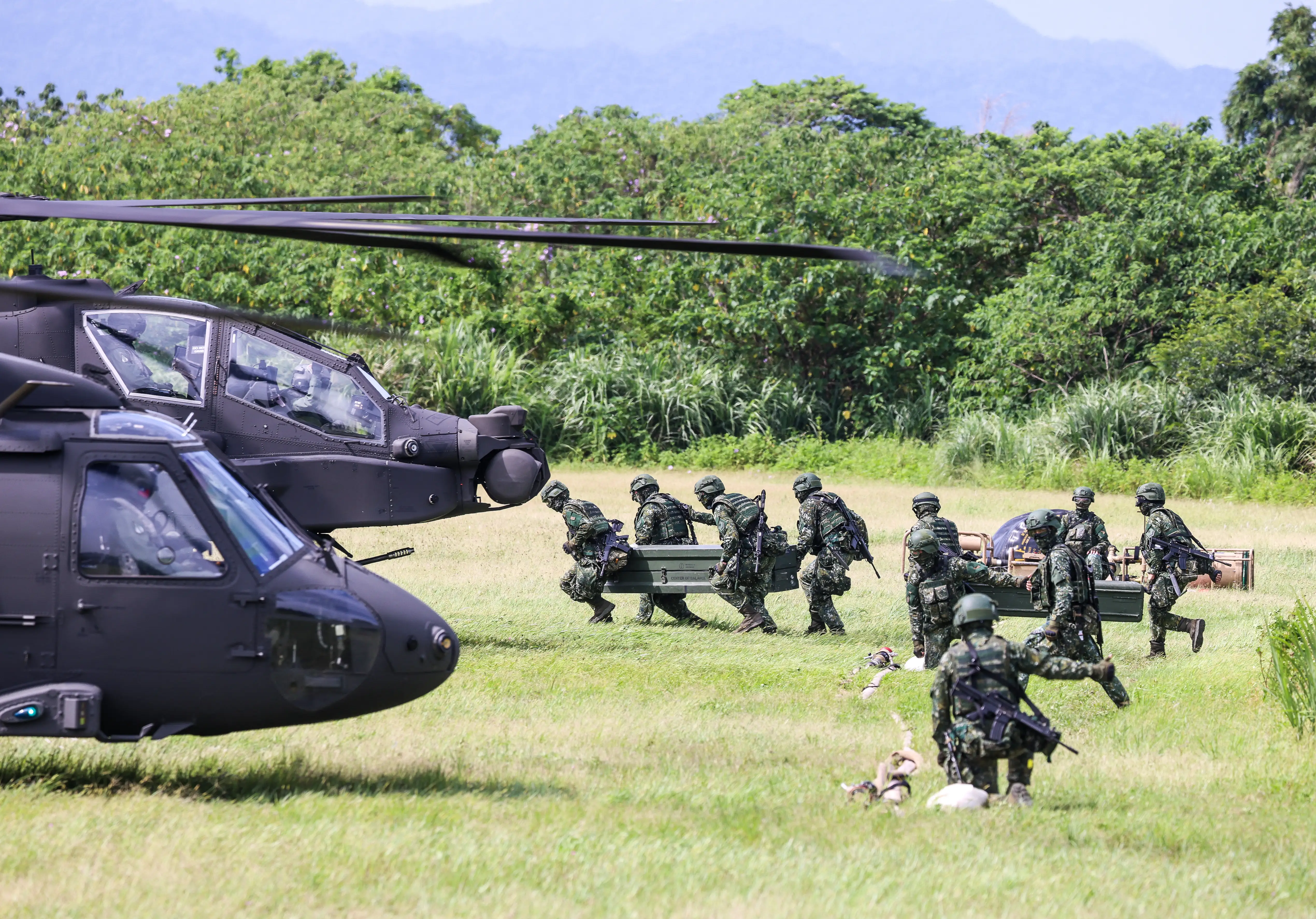 Taiawnese soldiers hoist fuel supplies and ammunition to helicopters in an open field.