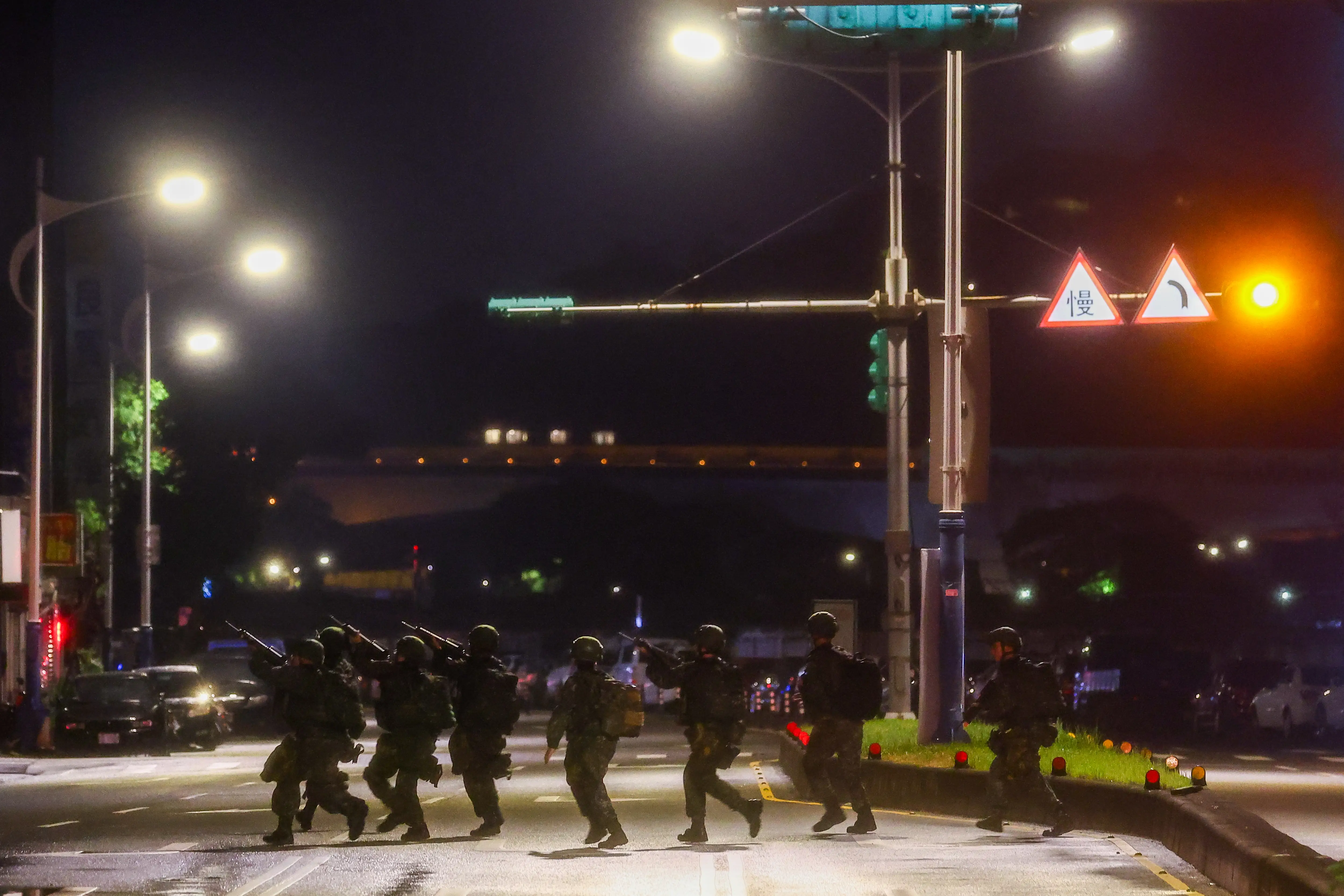A squad of Taiwanese infantry run across a street with rifles.