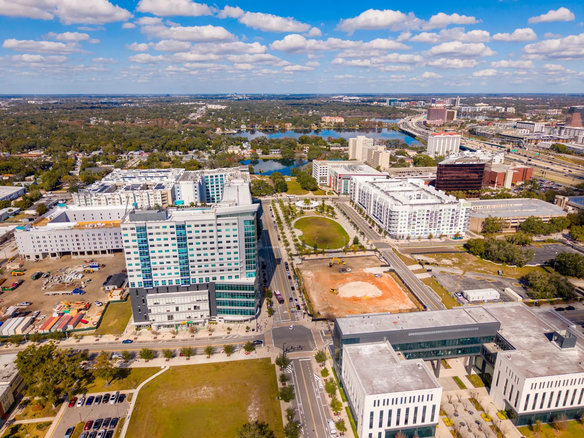 Aerial view of University of Central Florida UCF Downtown campus with high-rise buildings, roads, lakes, and a construction site under a cloudy sky.