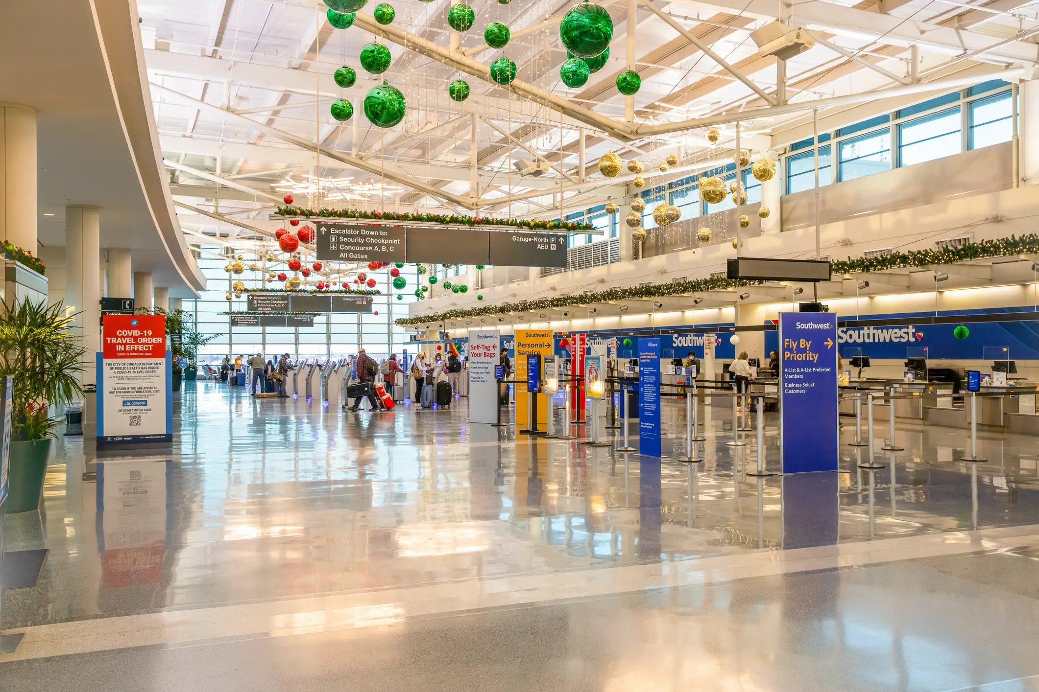 Bright airport check-in hall with Southwest counters, holiday ornaments, directional signs, and a COVID-19 travel order notice.
