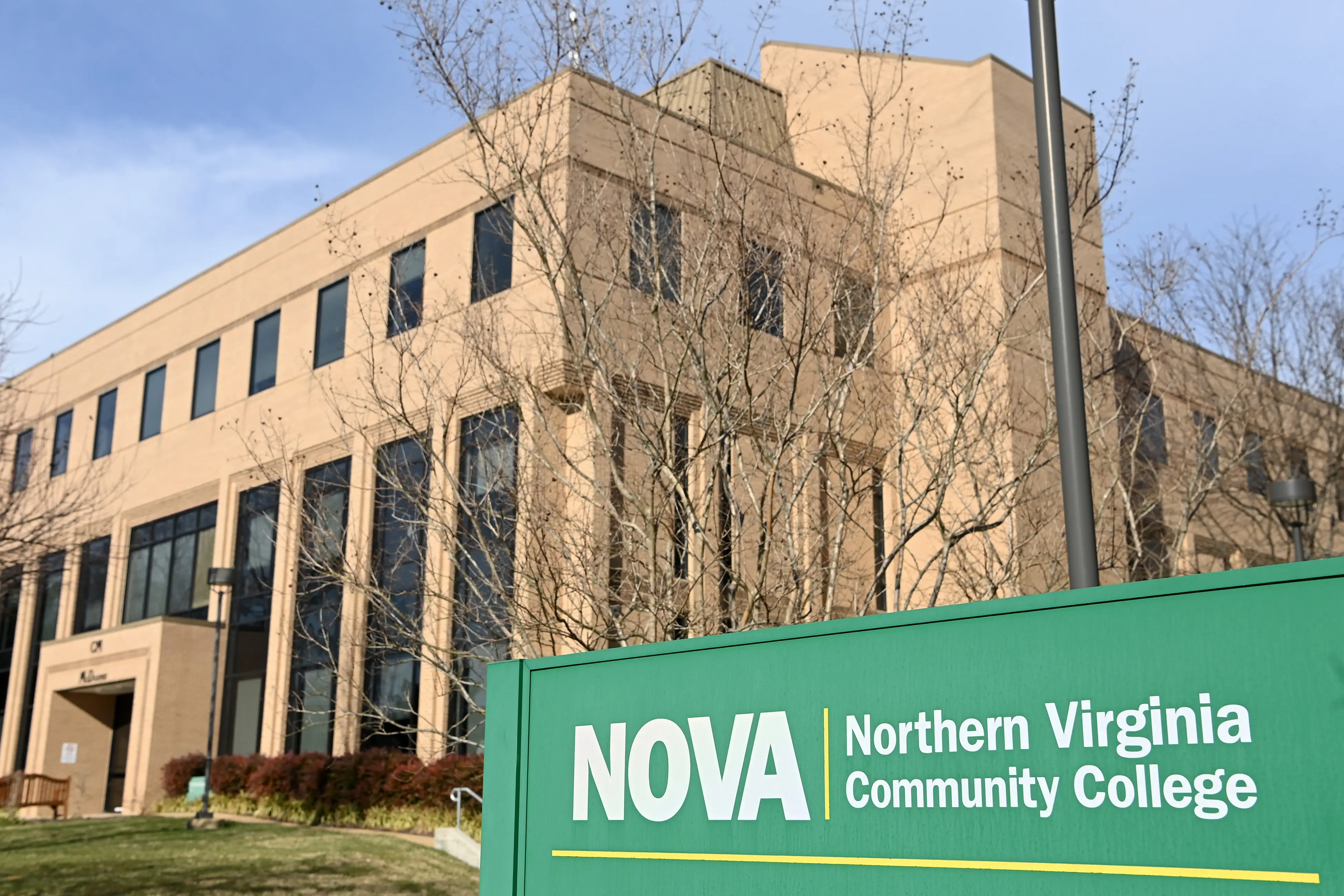 NOVA Northern Virginia Community College sign stands in front of a beige campus building with leafless trees.