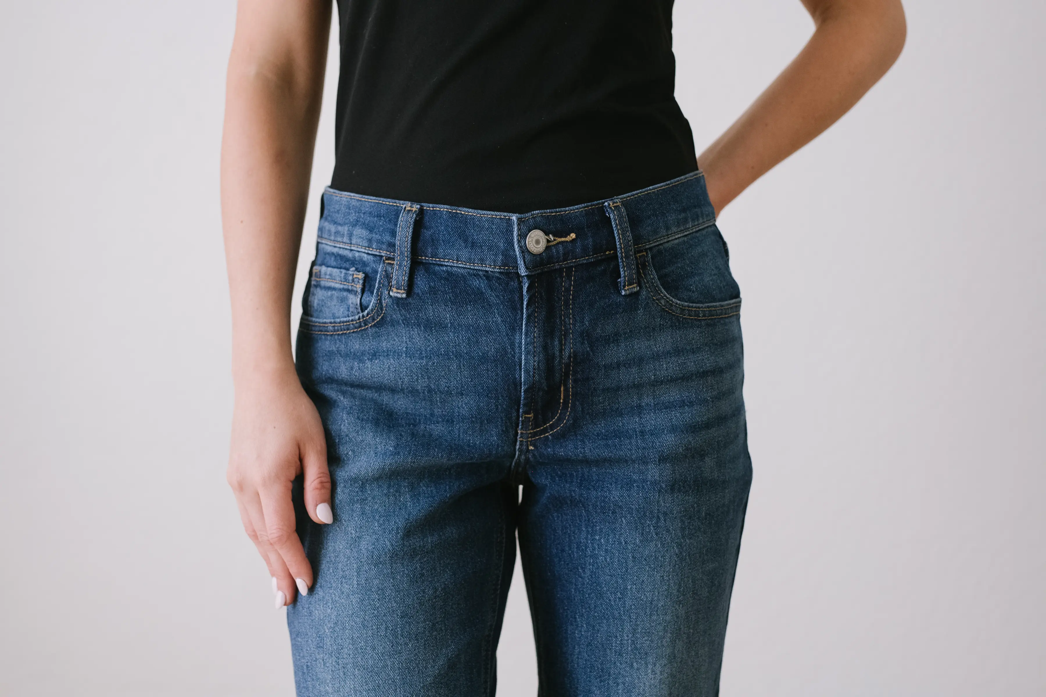Person wearing a black top and blue jeans stands against a plain light background.
