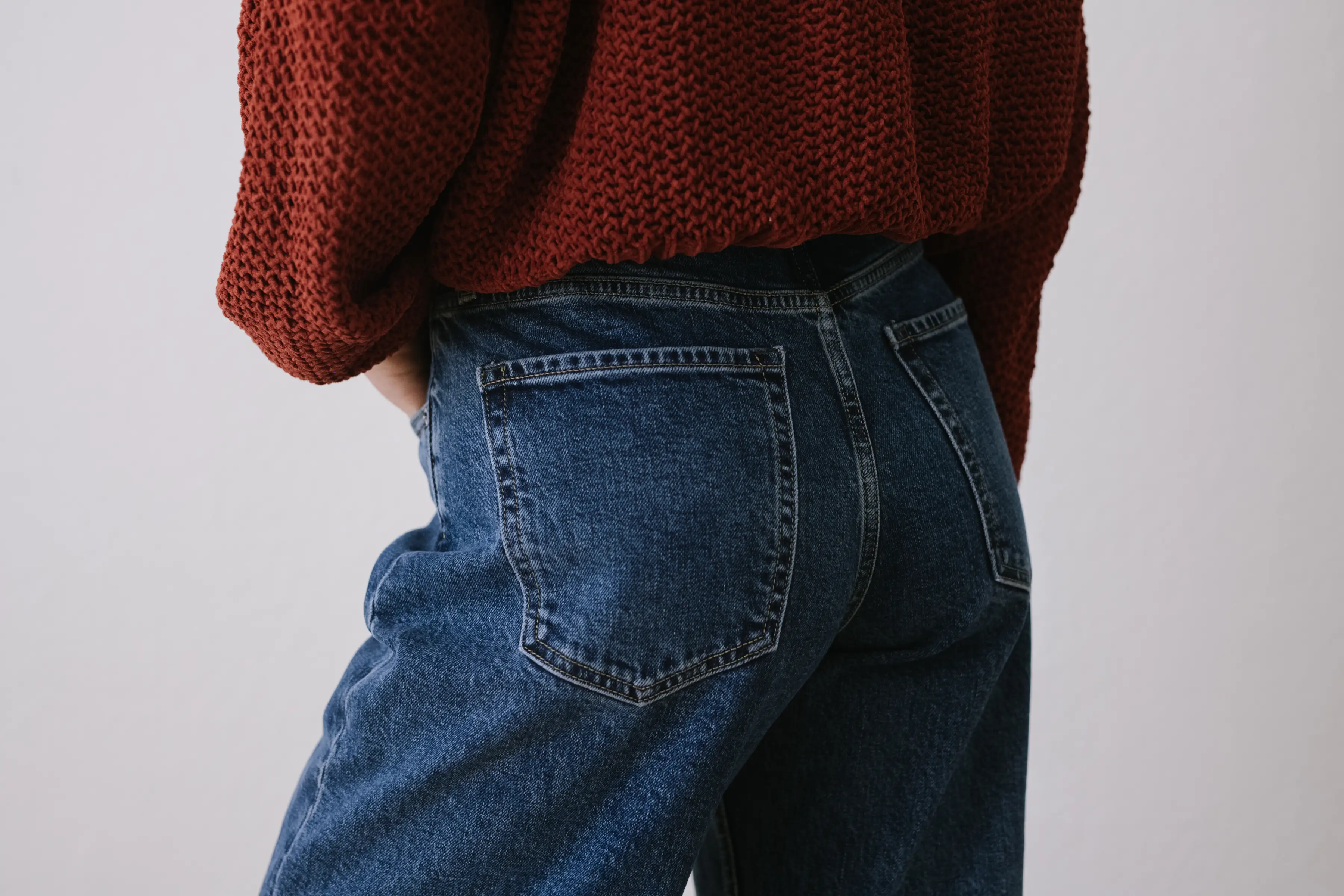 Close-up rear view of a person wearing a rust knit sweater and blue denim jeans.