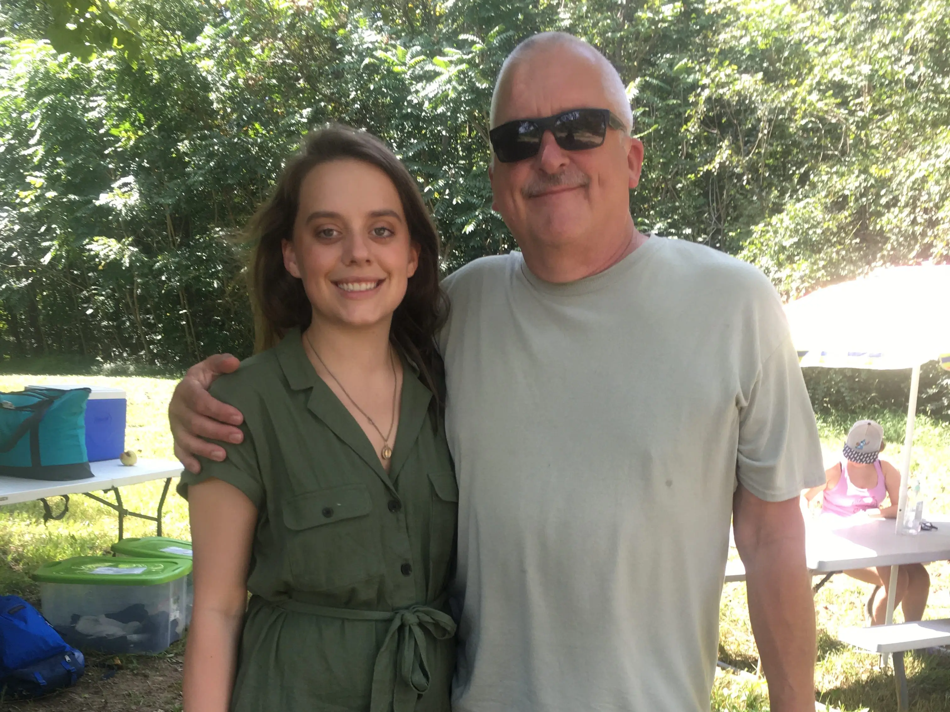 The writer and her dad standing side by side at an apple orchard, with trees and a picnic table in the background.