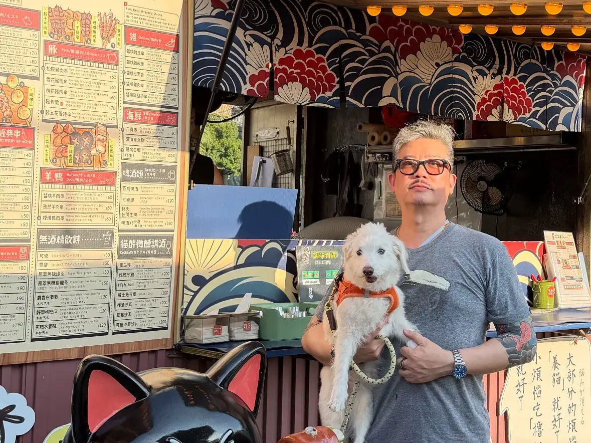 A man posing with his dog in front of a food truck in Taiwan.