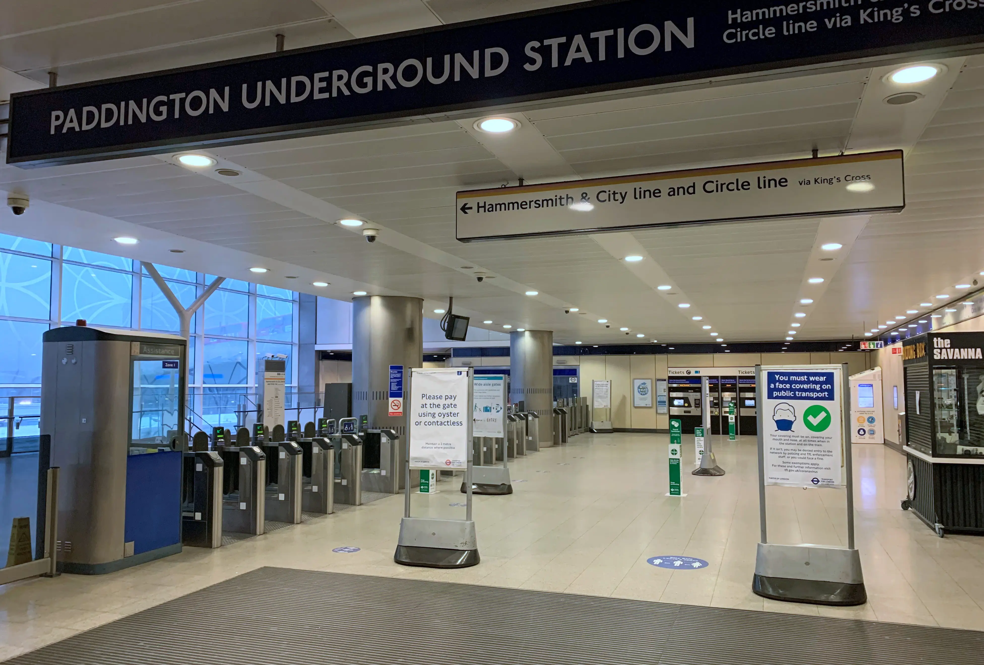 Paddington Underground Station concourse with ticket barriers, wayfinding signs, and face covering notices visible.