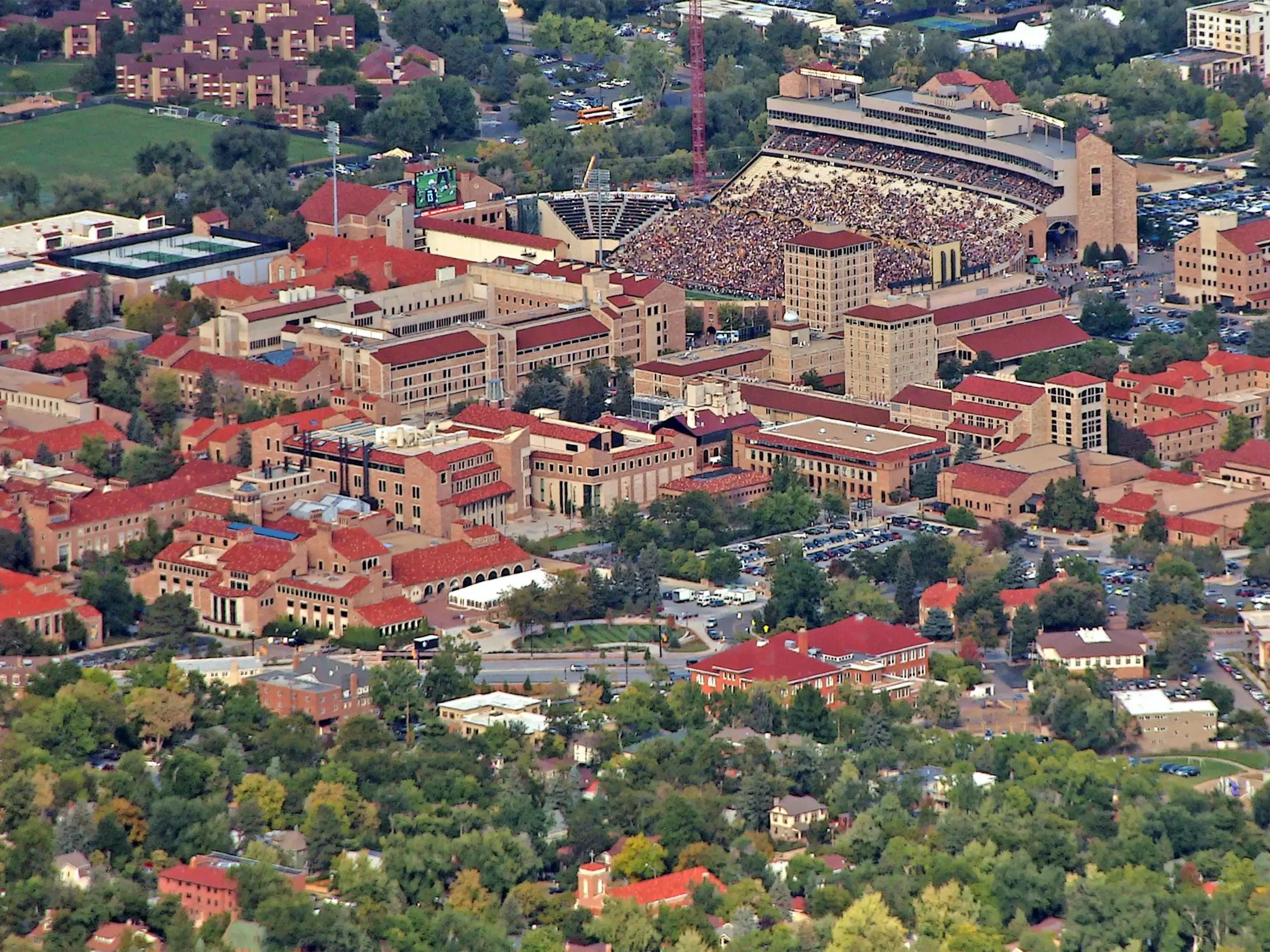Aerial view of the University of Colorado Boulder campus with a packed football stadium among red-roofed buildings.