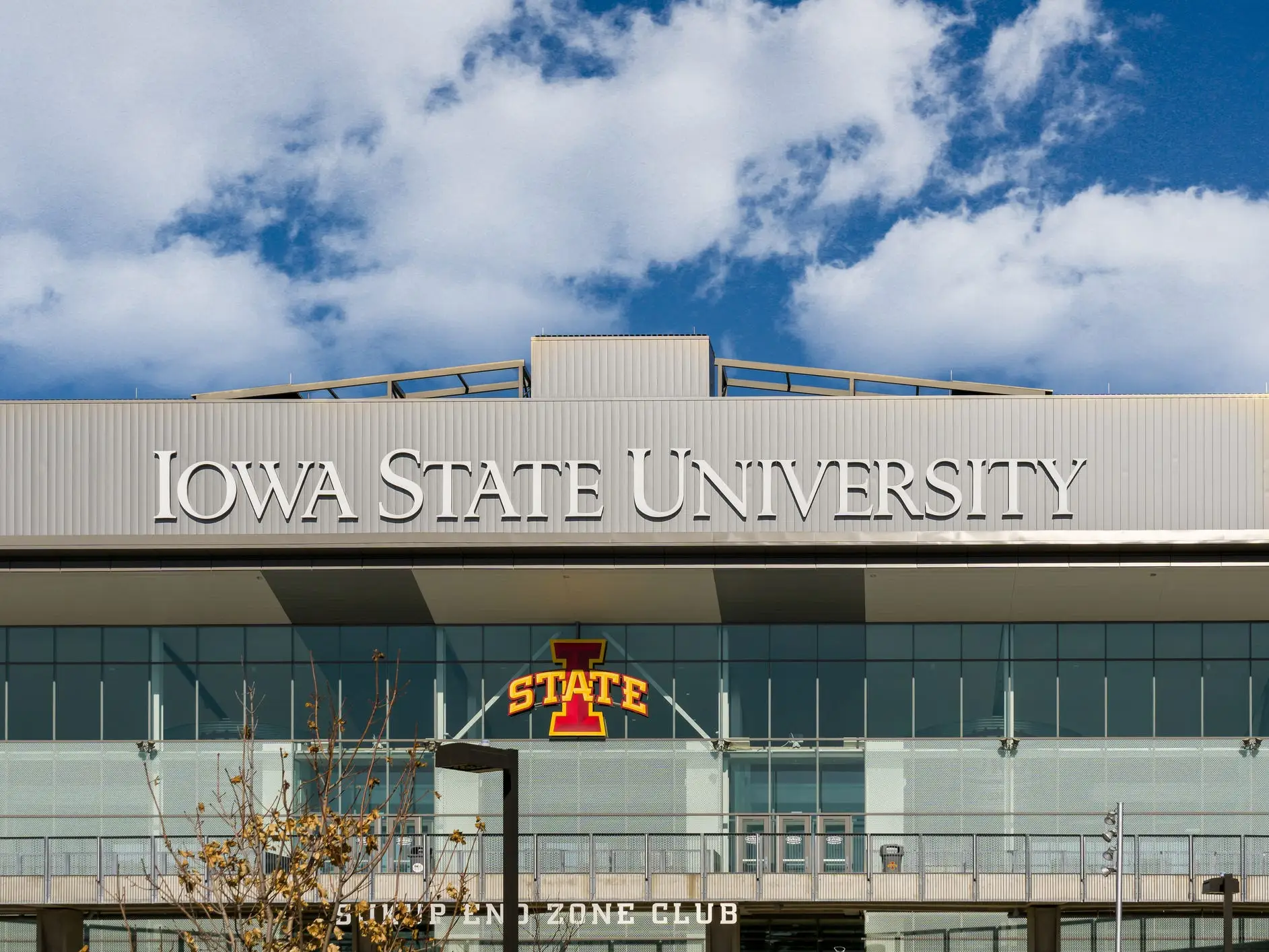 Iowa State University signage and the I-State logo appear on a modern stadium building under a partly cloudy sky.