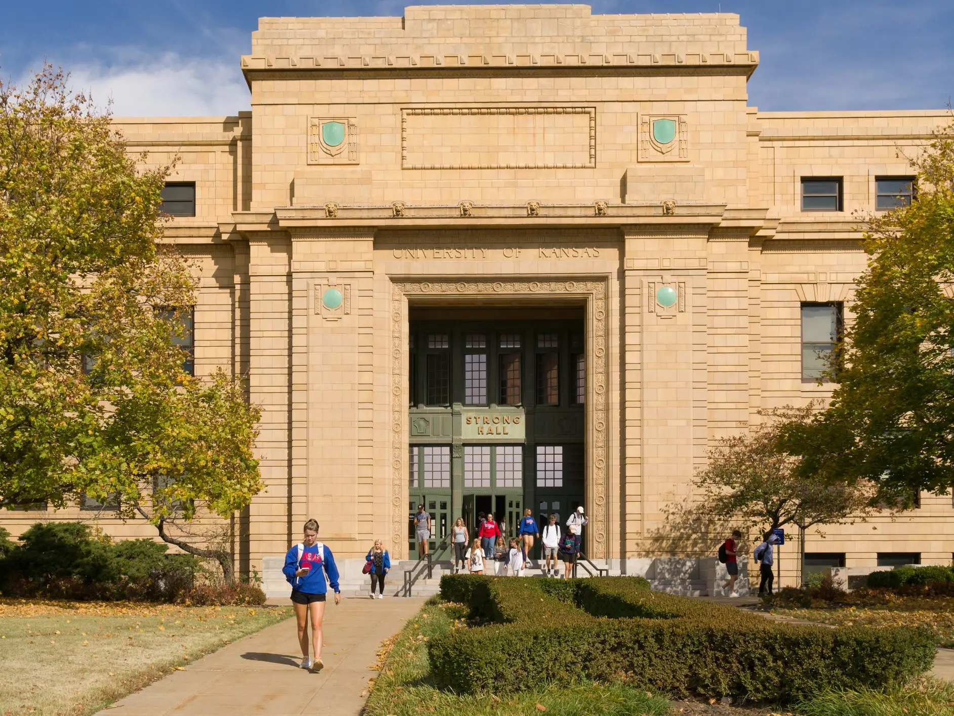 Students walk outside the University of Kansas Budig Hall and Hoch Auditorium entrance on a sunny campus day.