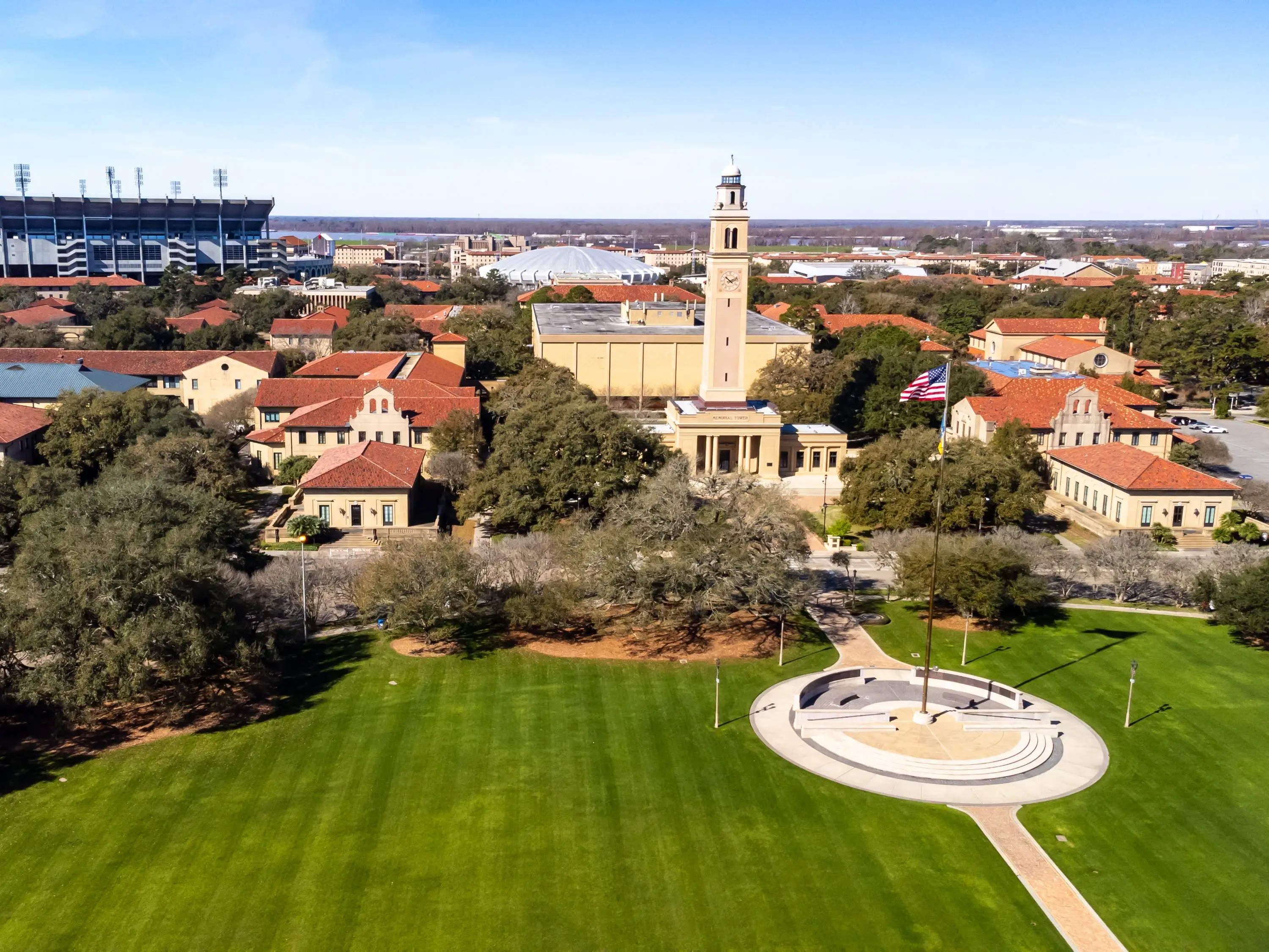 Aerial view of the Louisiana State University campus lawn, Memorial Tower, red-roofed buildings, and Tiger Stadium.