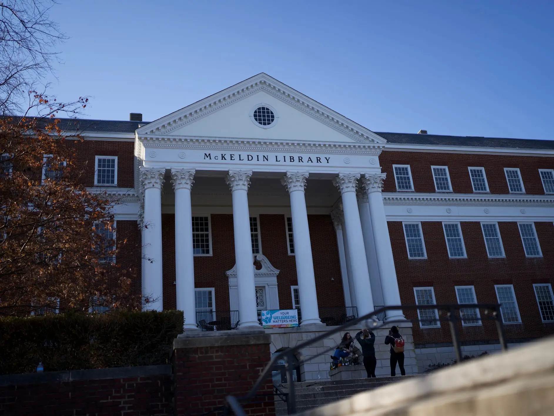 McKeldin Library's red brick facade and white columns stand under a clear blue sky with people on the steps.