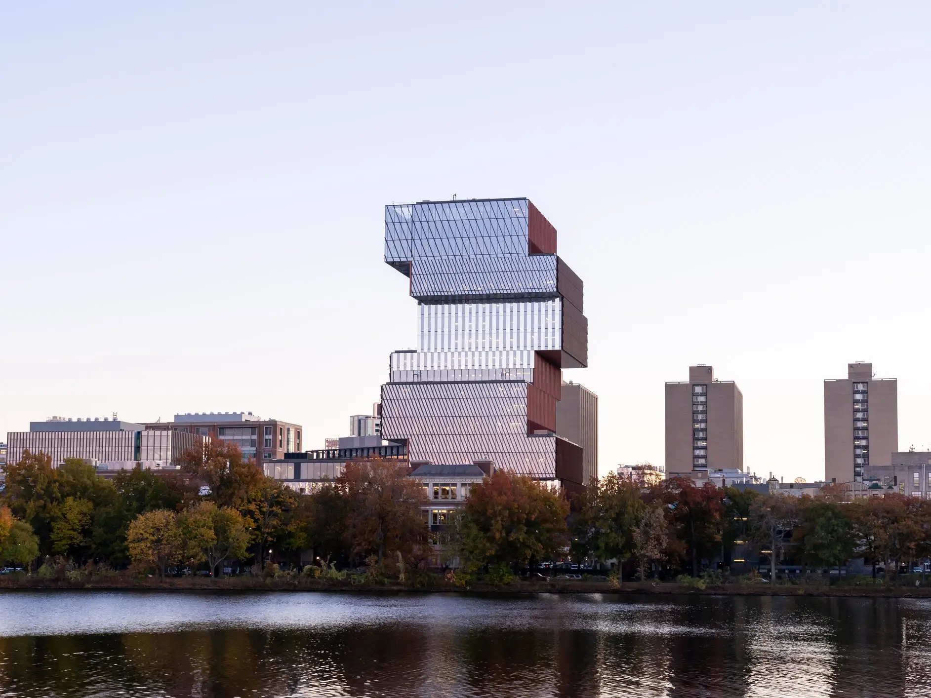 Boston University Center for Computing and Data Sciences rises behind autumn trees beside a reflective river at dusk.