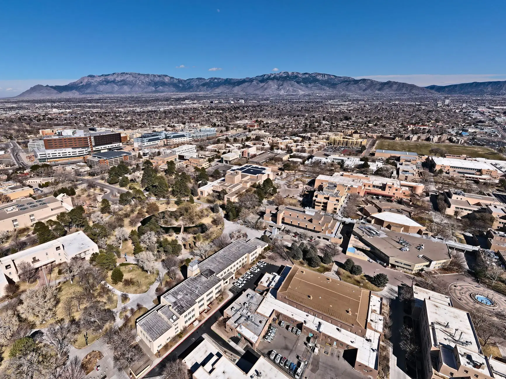 Aerial view of the University of New Mexico campus and the surrounding city with a mountain range under a clear blue sky.