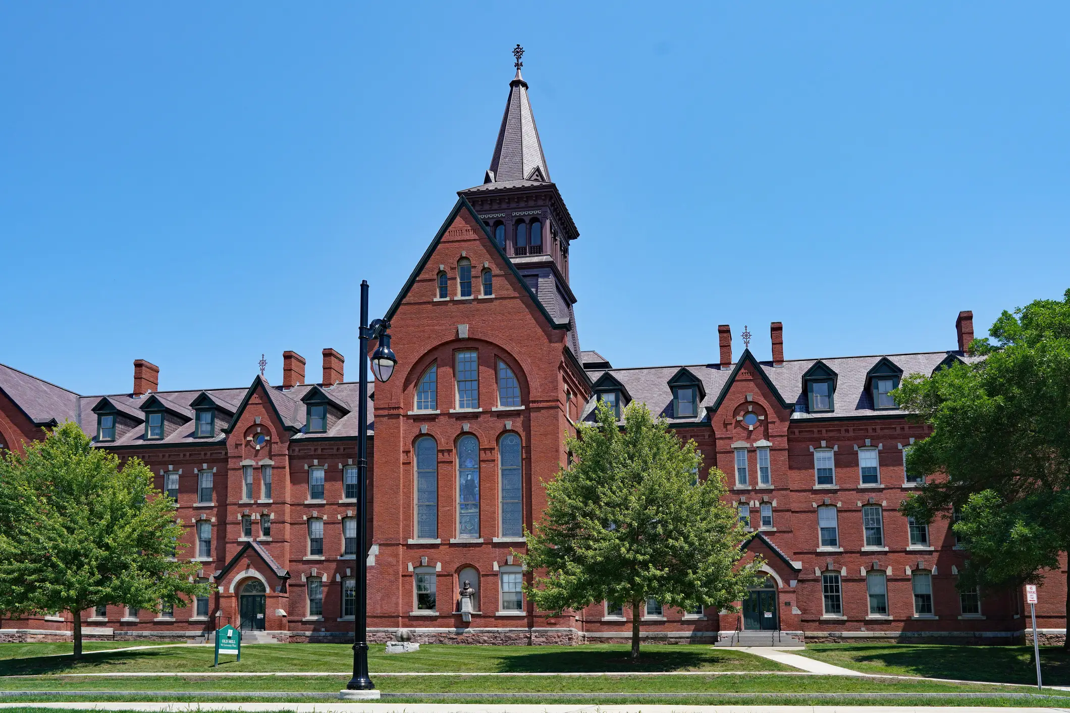 Red brick campus building with a central tower and trees under a clear blue sky.