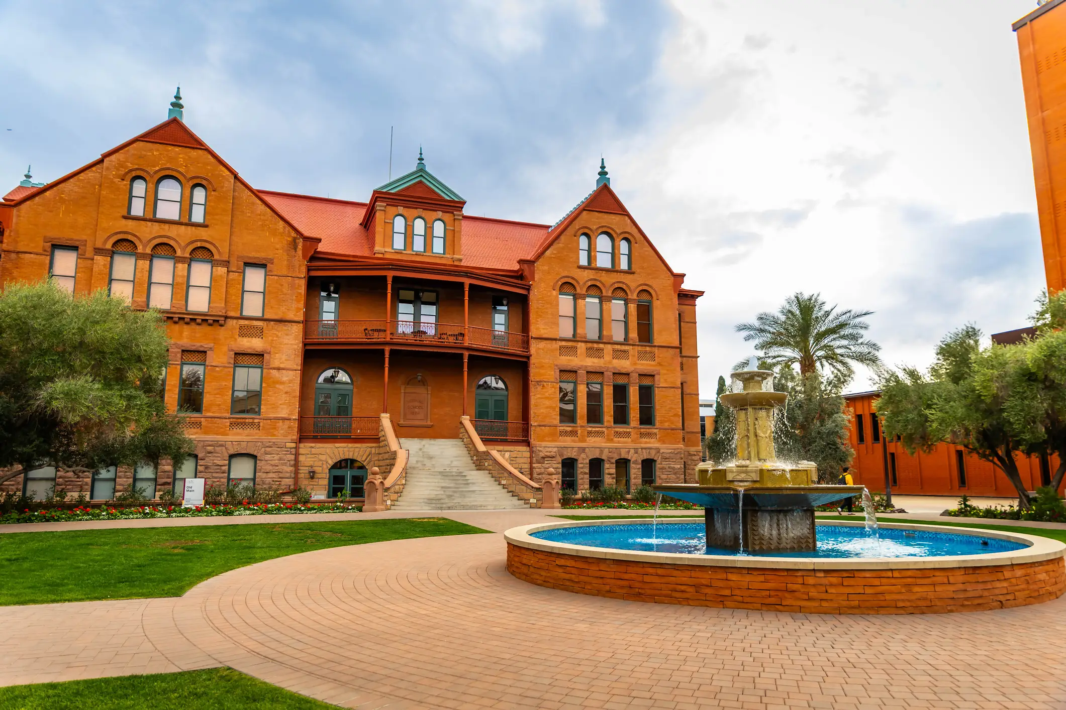 Historic red-brick Old Main building at Arizona State University stands behind a courtyard fountain and landscaped lawn.