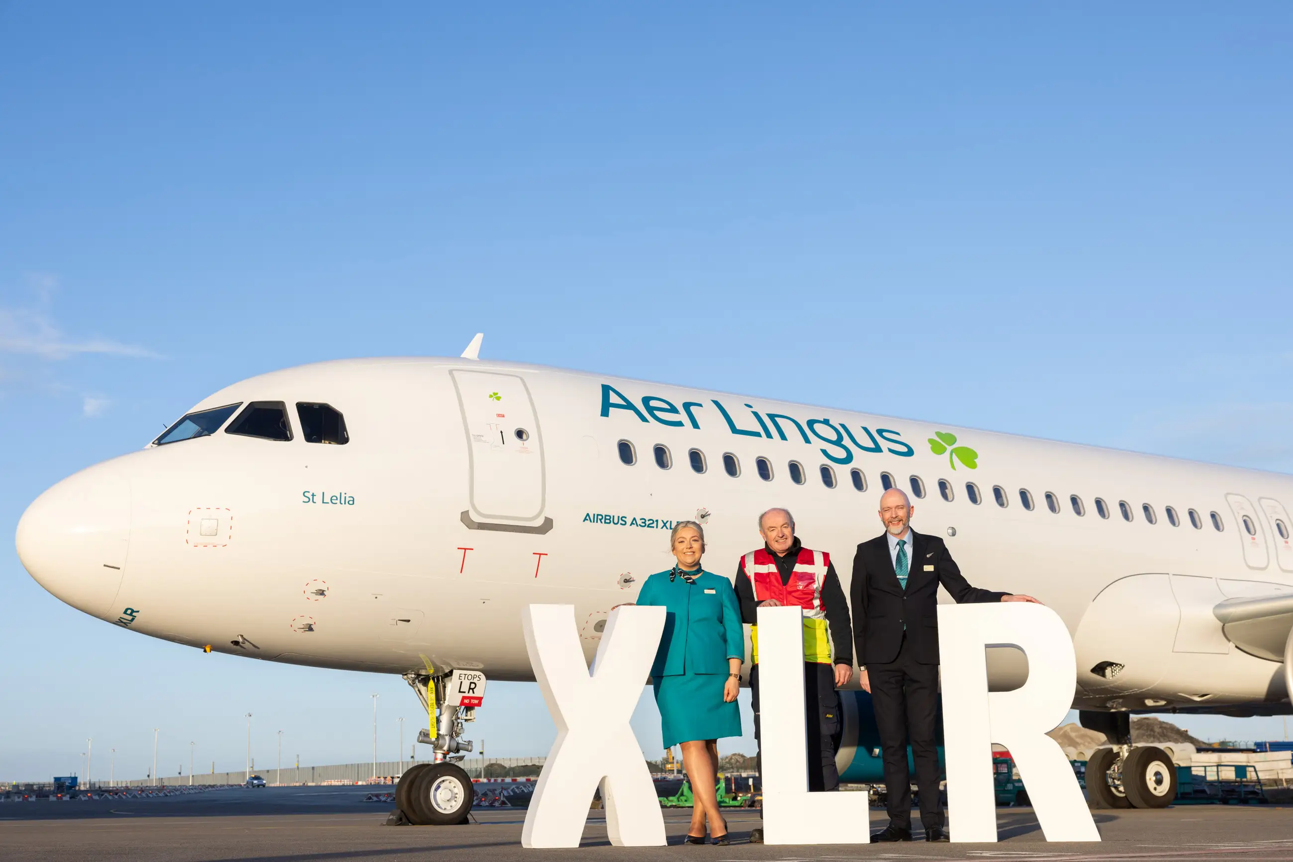 Aer Lingus staff stand in front of letters spelling XLR and the airline's first Airbus A321XLR airplane.